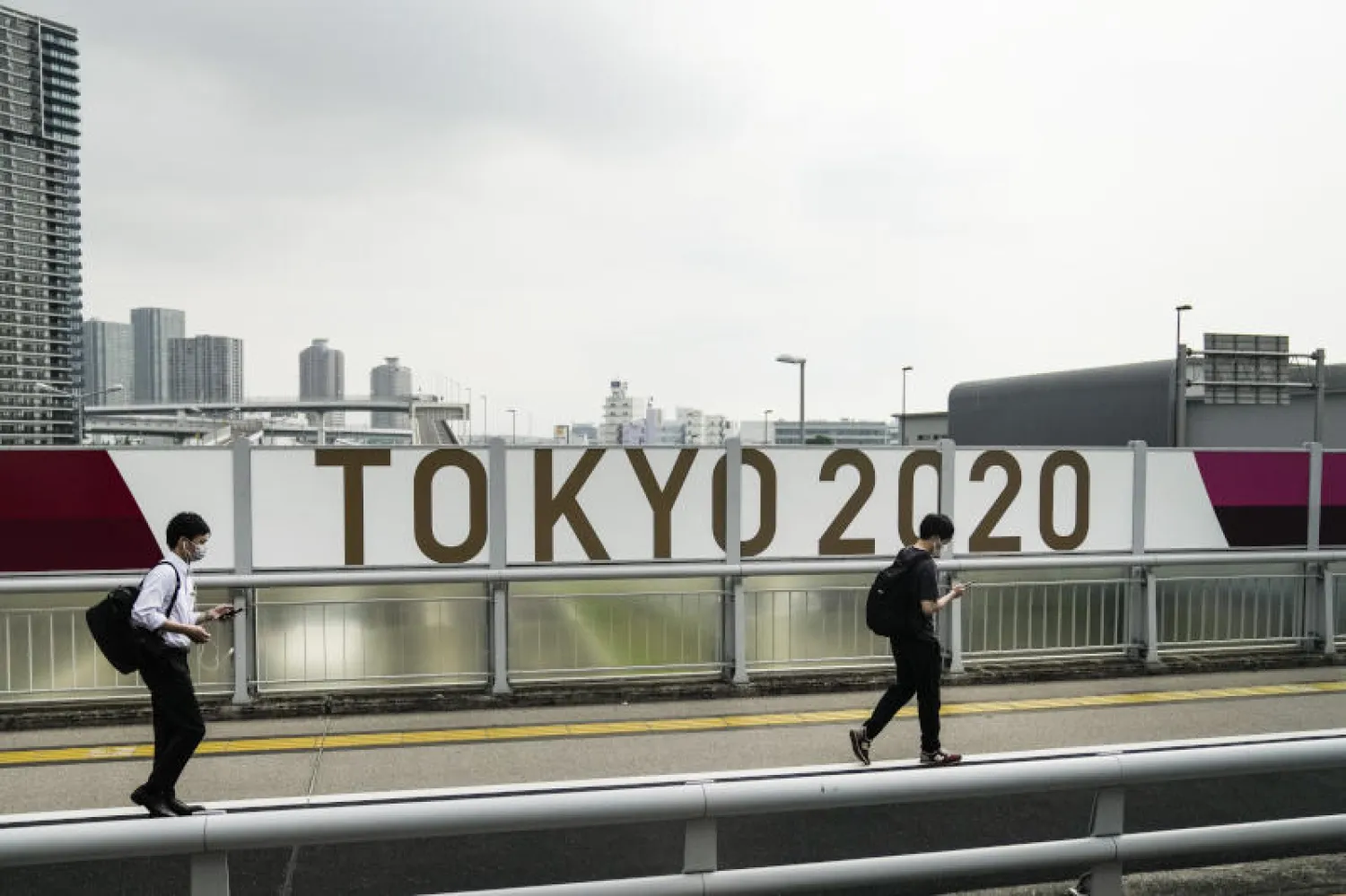 رجلان يمران أمام شعار ألعاب طوكيو 2020 في العاصمة اليابانية (أ.ب)
