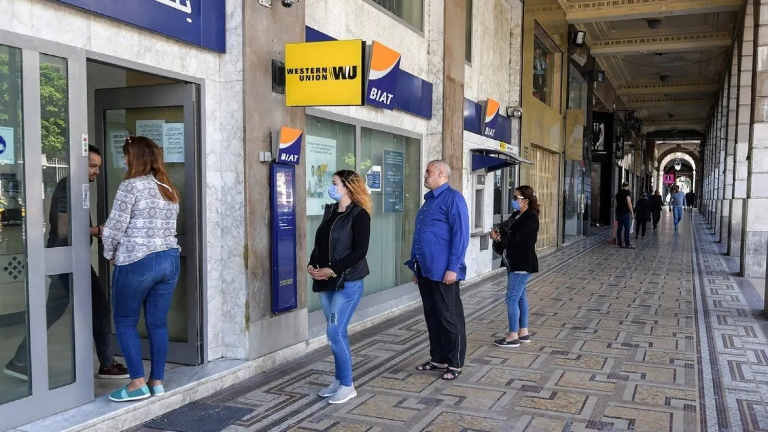 Tunisians, some wearing face masks, due to coronavirus pandemic queue up to enter a bank branch in the center of the Tunisian capital Tunis on May 4, 2020. (AFP)
