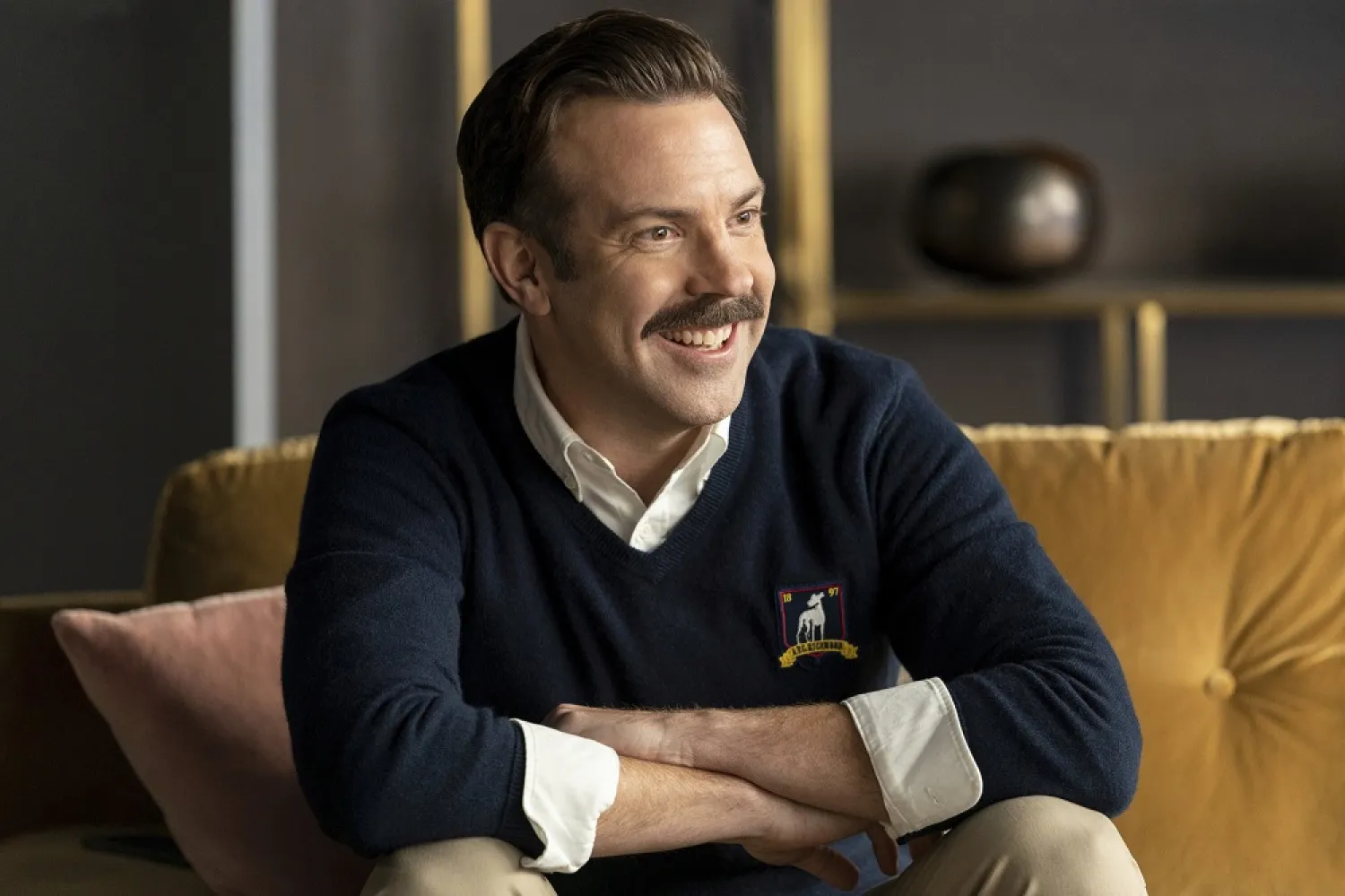 Jason Sudeikis, as Ted Lasso, smiles as he sits on a sofa, in a scene from the series. (Apple TV+ via AP)