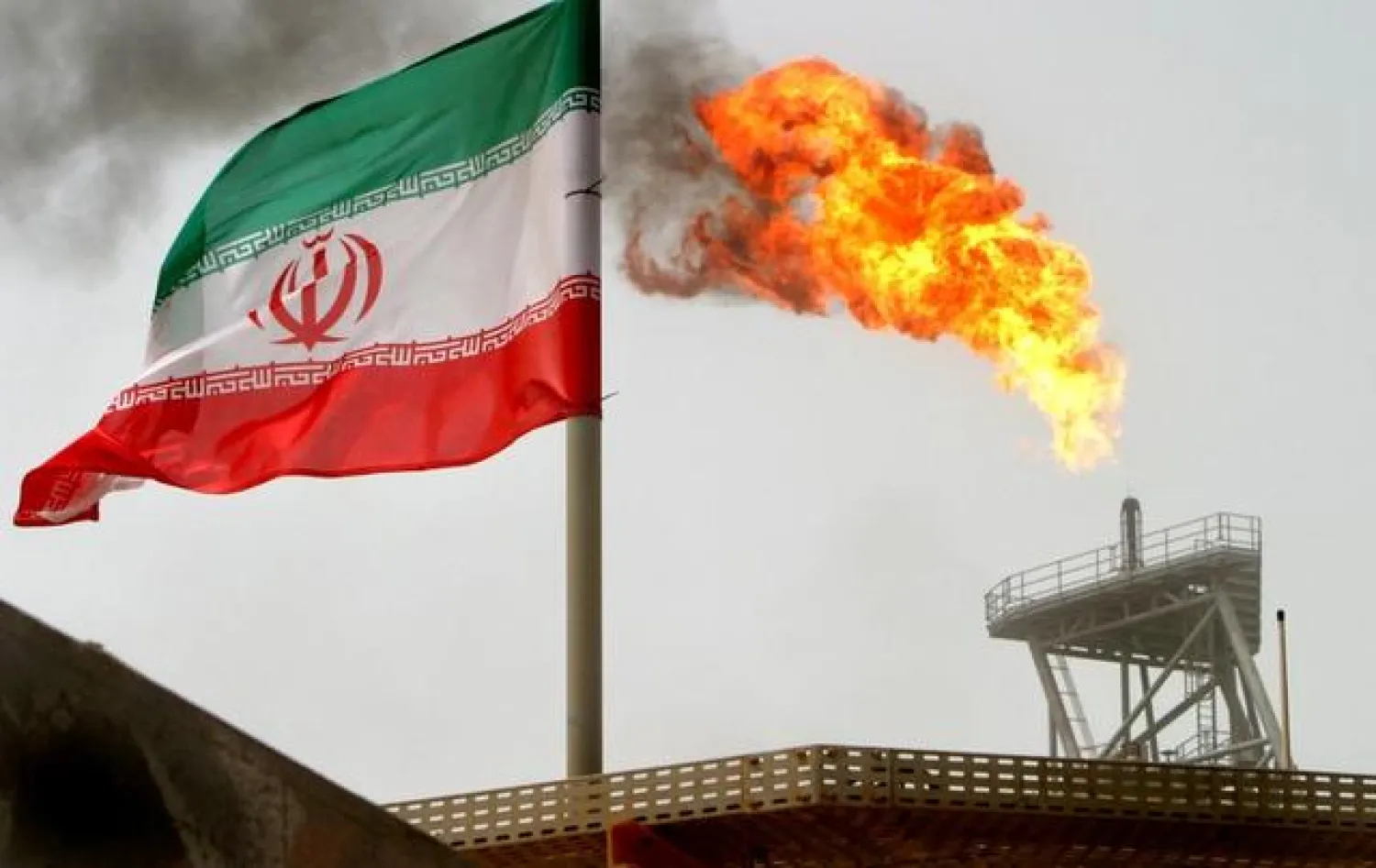 A gas flare on an oil production platform is seen alongside an Iranian flag in the Gulf July 25, 2005. REUTERS/Raheb Homavandi/File Photo