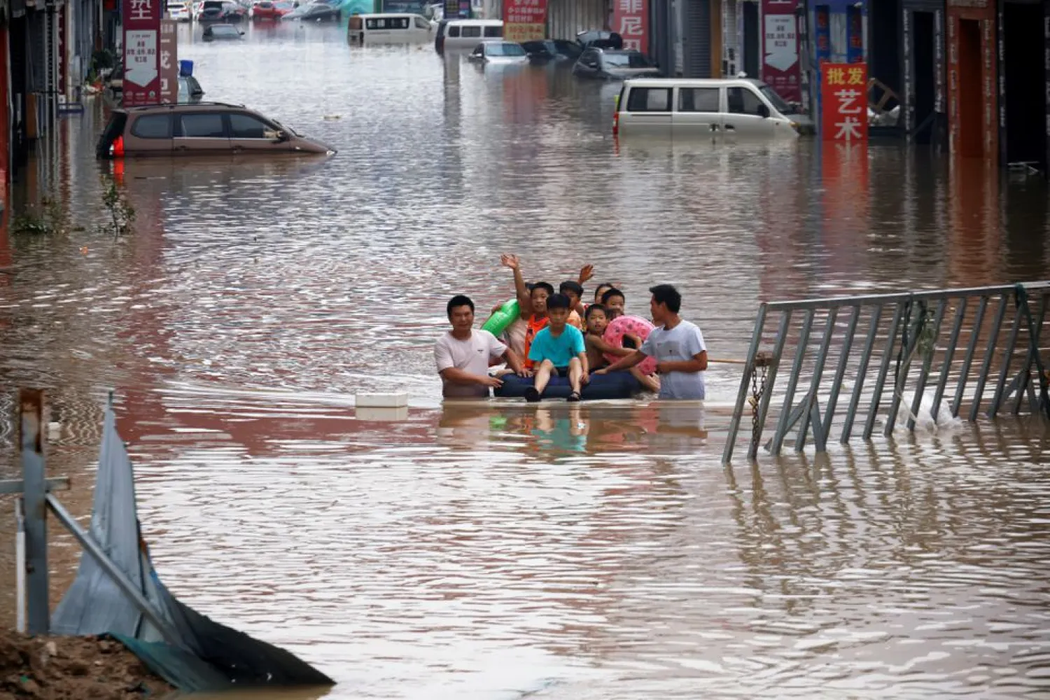 Children sit on a makeshift raft on a flooded road following heavy rainfall in Zhengzhou, Henan province, China July 22, 2021. REUTERS/Aly Song/File Photo
