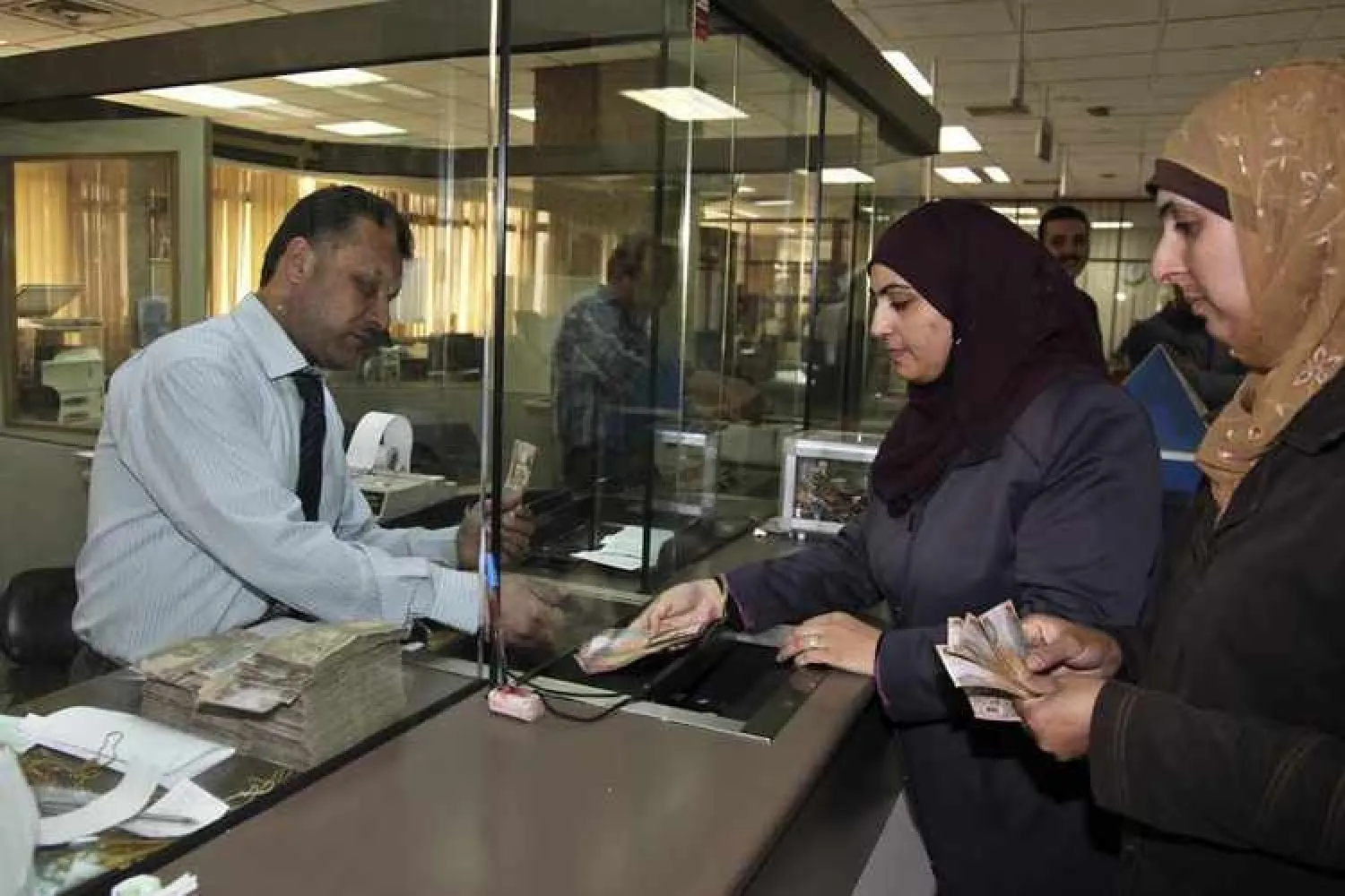 Image used for illustrative purpose. Customers (R) deposit Jordanian dinars at the Jordan Islamic Bank in Amman. REUTERS/Majed Jaber