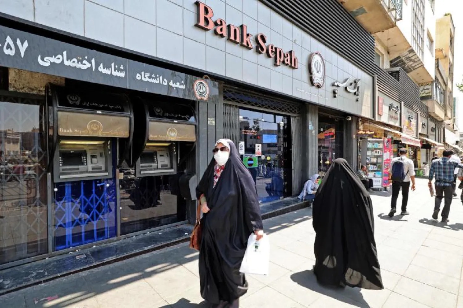 امرأة إيرانية ترتدي قناعًا وقائيًا للوجه تمر أمام فرع بنك  في وسط مدينة طهران(ا.ف.ب)