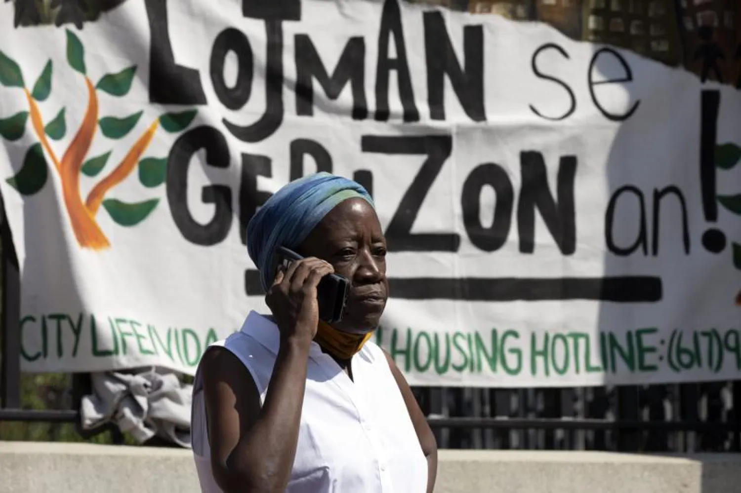 A woman speaks on the phone in front of a sign in Haitian Creole during a news conference held by a coalition of housing justice groups to protest evictions, Friday, July 30, 2021, outside the Statehouse in Boston. (AP Photo/Michael Dwyer)
