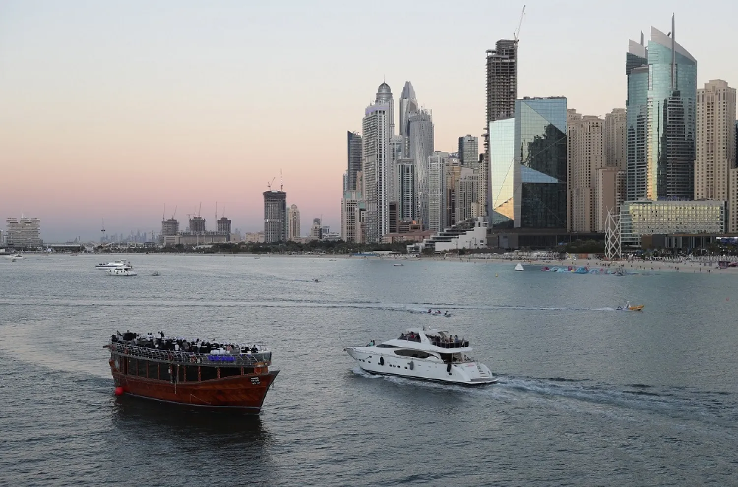 Tourists on a yacht as they pass a traditional dhow serving a dinner cruise, in Dubai, United Arab Emirates, Tuesday, Jan. 12, 2021 (AP)