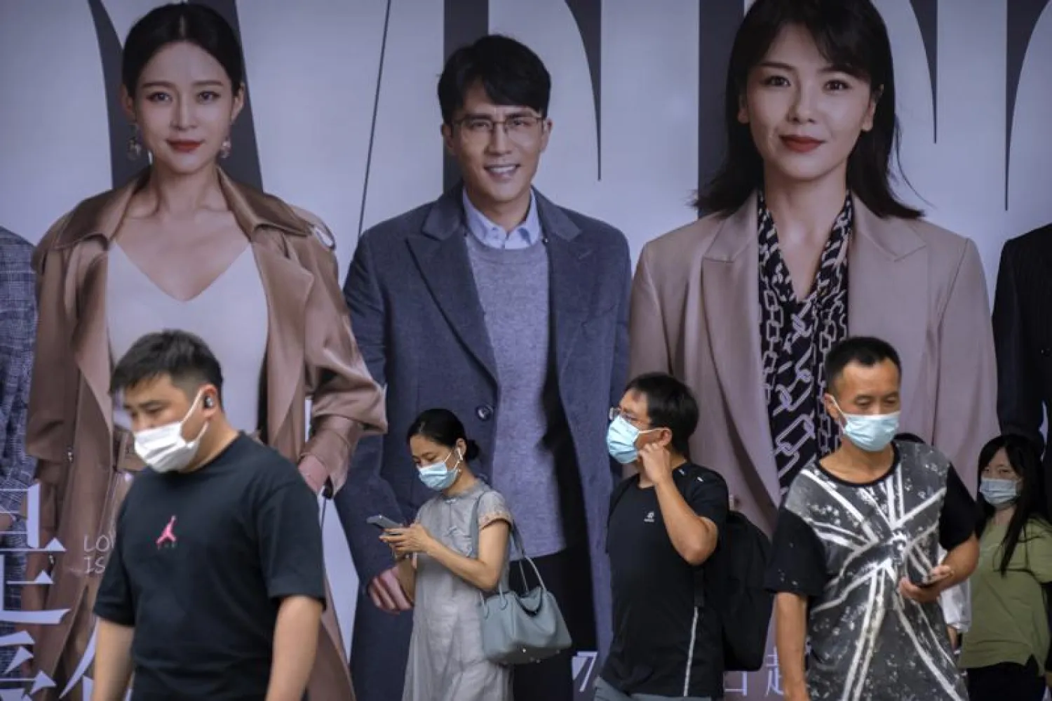 People wearing face masks to help protect against COVID-19 walk past an advertising billboard at a subway station during the morning rush hour in Beijing, Wednesday, Aug. 4, 2021. (AP Photo/Mark Schiefelbein)
