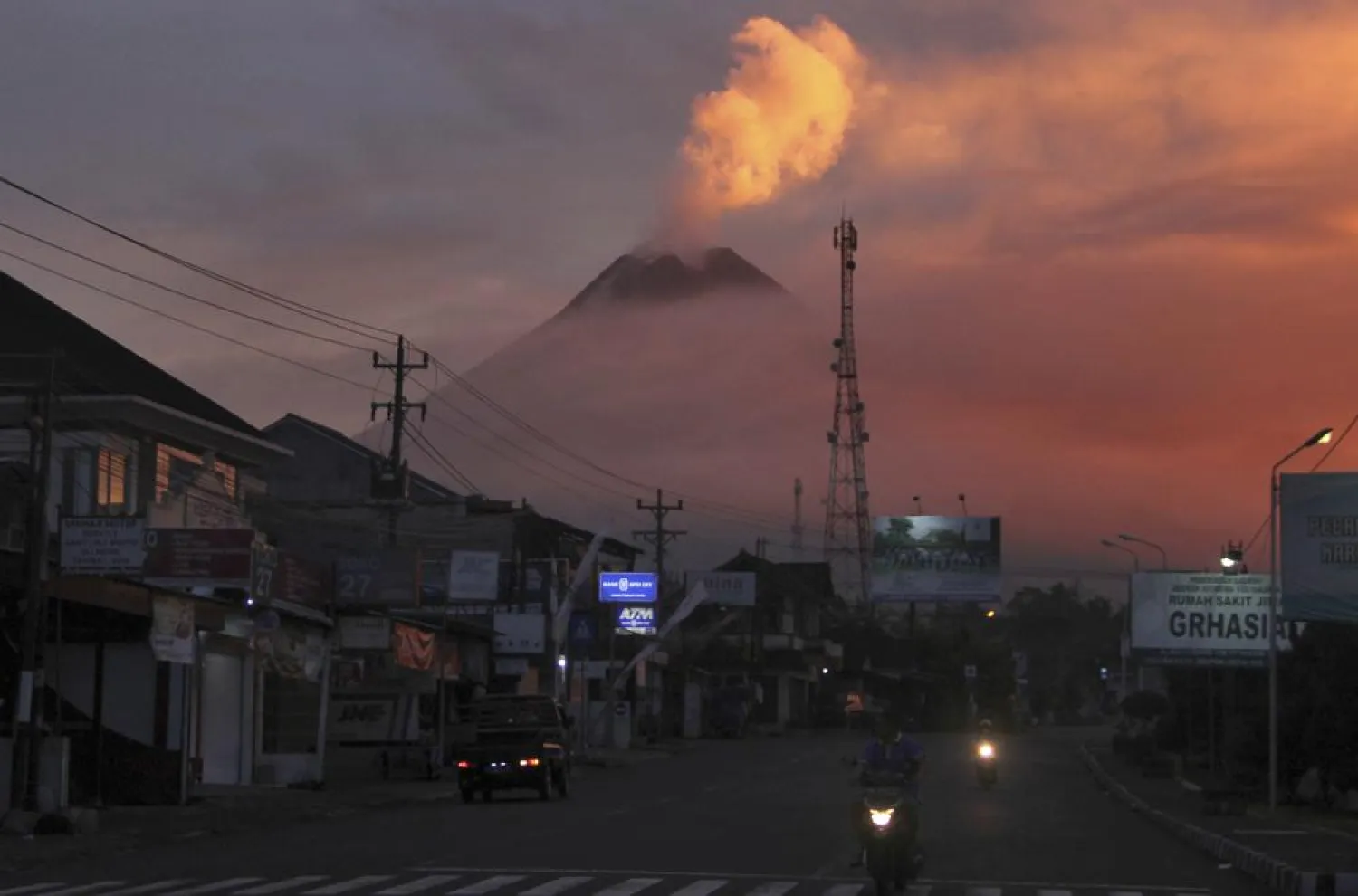 Motorists ride past as Mount Merapi looms in the background, in Sleman, Friday, June 25, 2021. (AP Photo/Slamet Riyadi)
