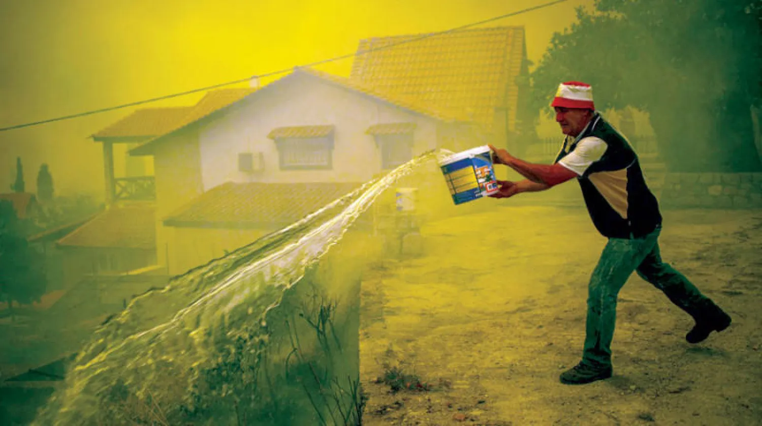 أحد سكّان قرية إيفيا يكافح ألسنة النار أمس (أ.ف.ب)