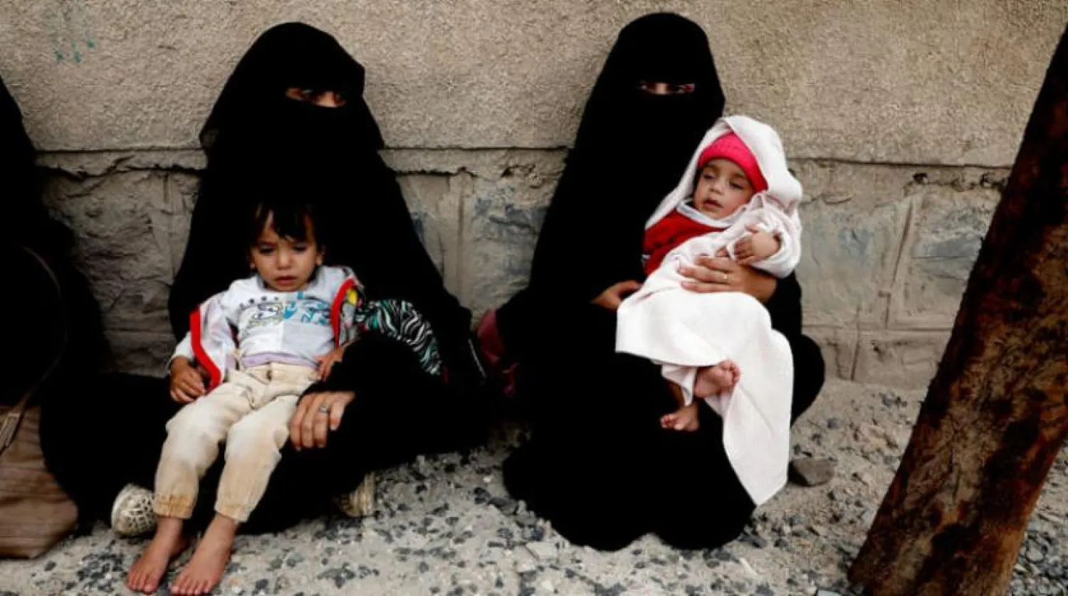 Two Yemeni women carry two children near a charitable organization in Sana’a (EPA)