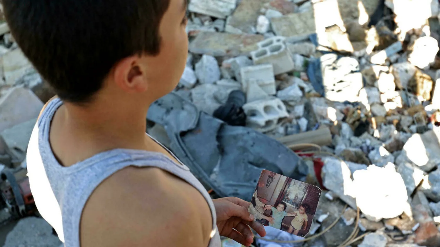 A boy holds a personal photo print showing children as he stands by rubble in the aftermath of Syrian government bombardment on Balashun in the Jabal al-Zawiya region in Idlib. (AFP)