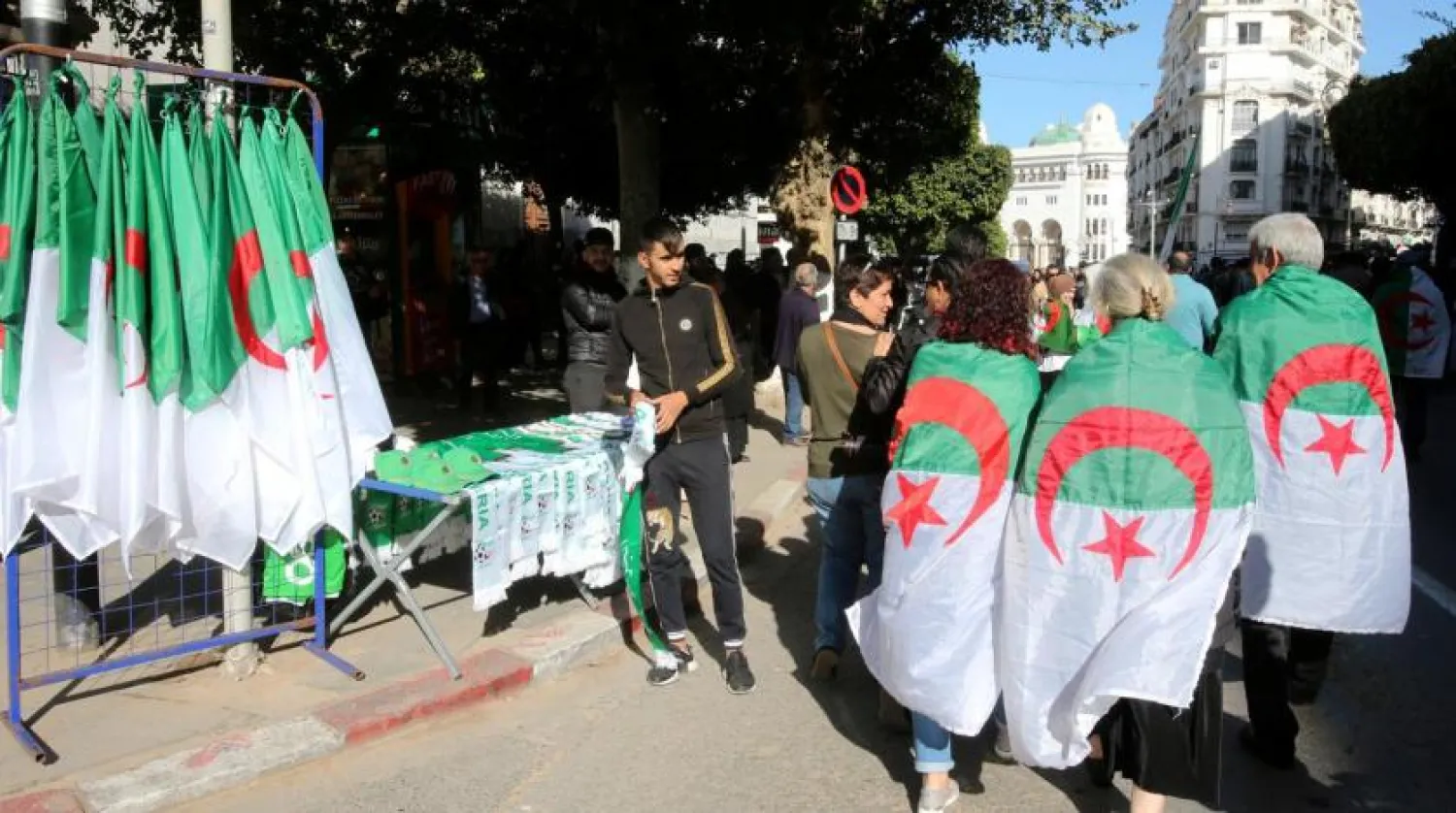 Demonstrators wearing national flags walk past a street vendor during a protest demanding a change of the power structure in Algiers, Algeria January 24, 2020. (Reuters)
