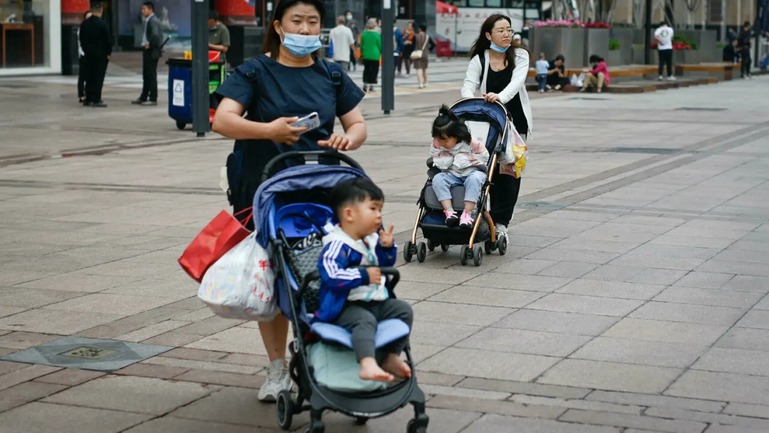 Two women push strollers along a business street in Beijing on May 31, 2021. (AFP)