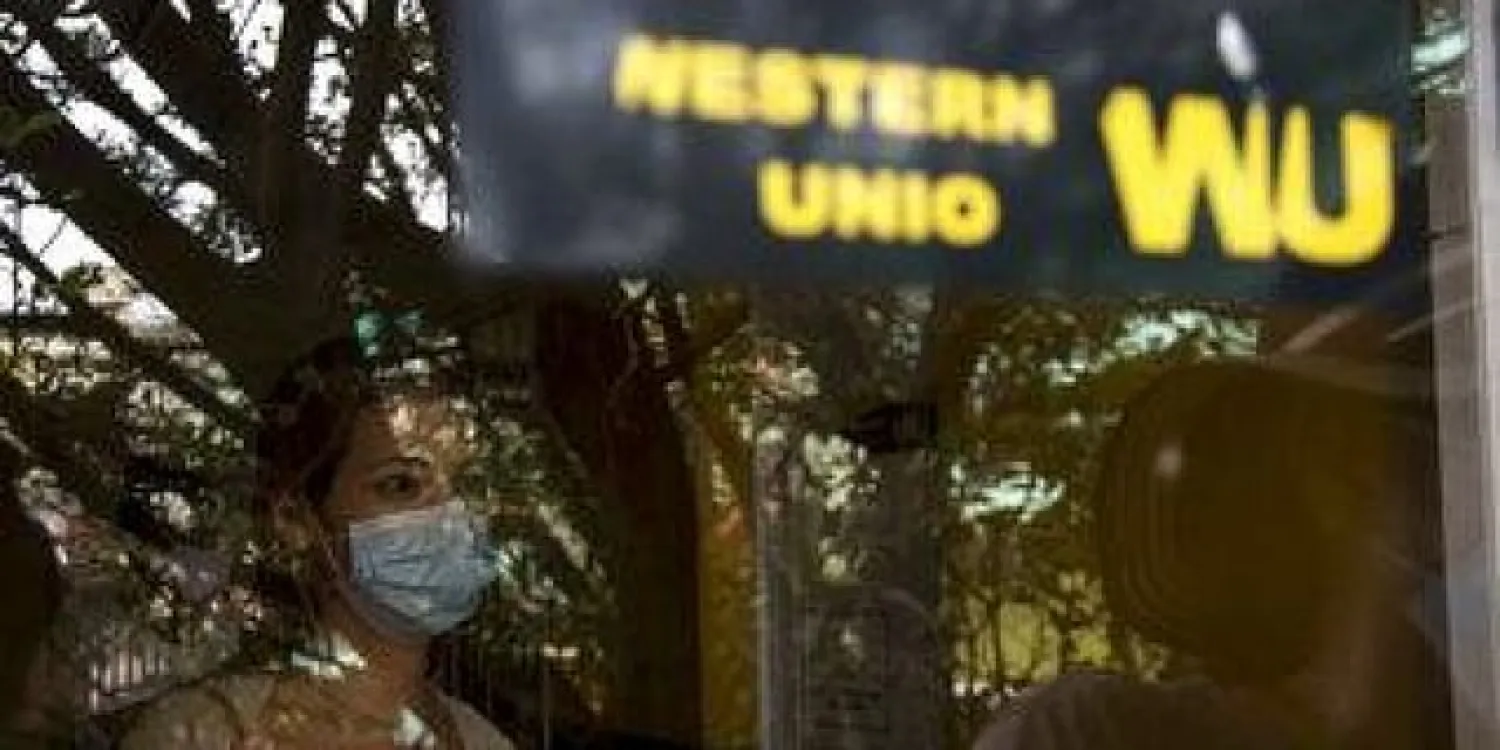 Photographed through a window, a woman waits to collect money at a Western Union office. (File Photo | AP)