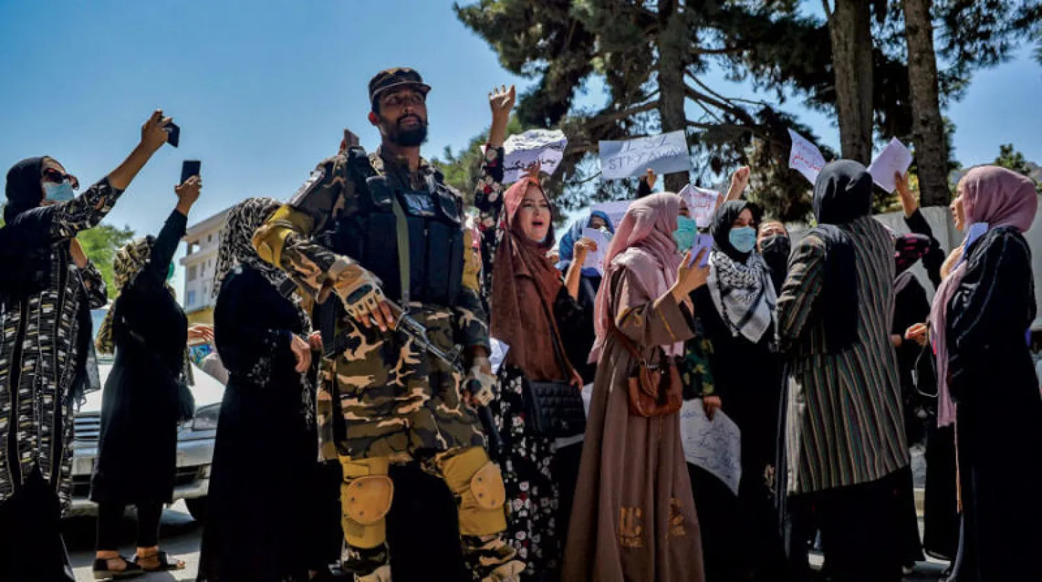 مقاتل من «طالبان» يقف أمام نساء تظاهرن قرب السفارة الباكستانية في كابل أمس (أ.ف.ب)