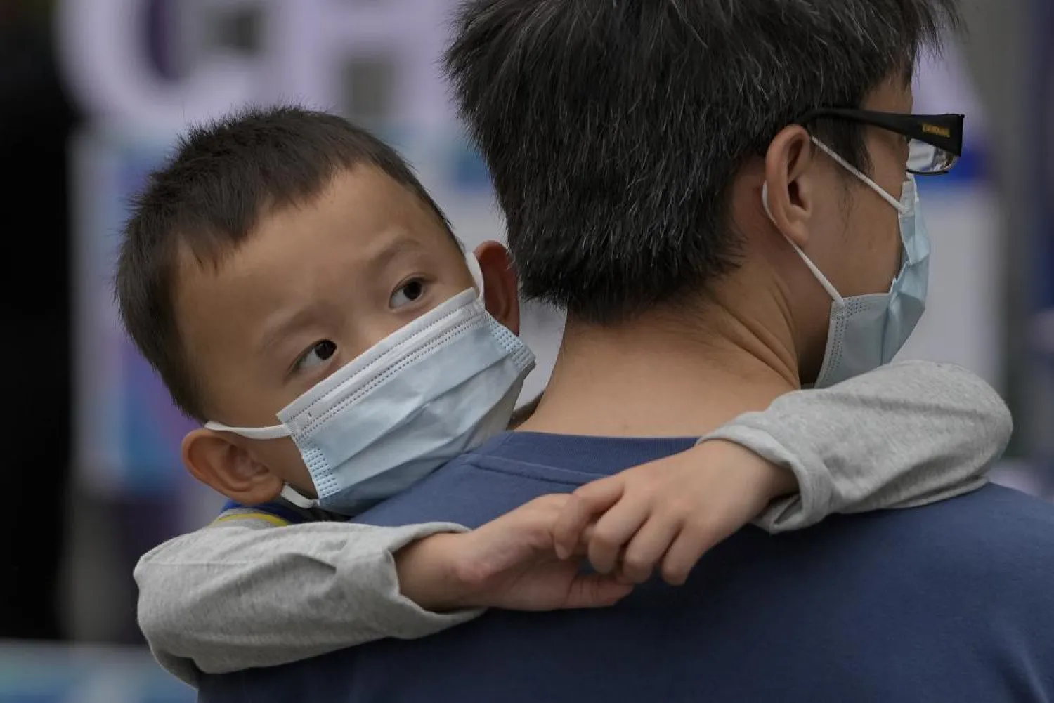 A man carries a child, both wearing face masks to help curb the spread of the coronavirus, walk on a street in Beijing, Sunday, Sept. 12, 2021. (AP Photo/Andy Wong)
