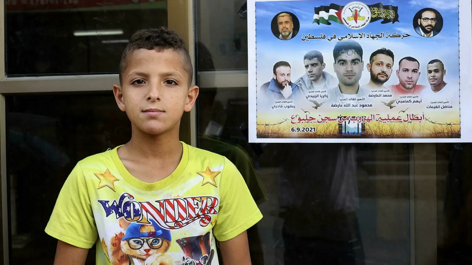 A Palestinian boy stands next to a poster showing the six Palestinian prisoners who escaped from Israel’s Gilboa prison, before four were recaptured, at the Jenin camp for Palestinian refugees in the occupied West Bank. (AFP)
