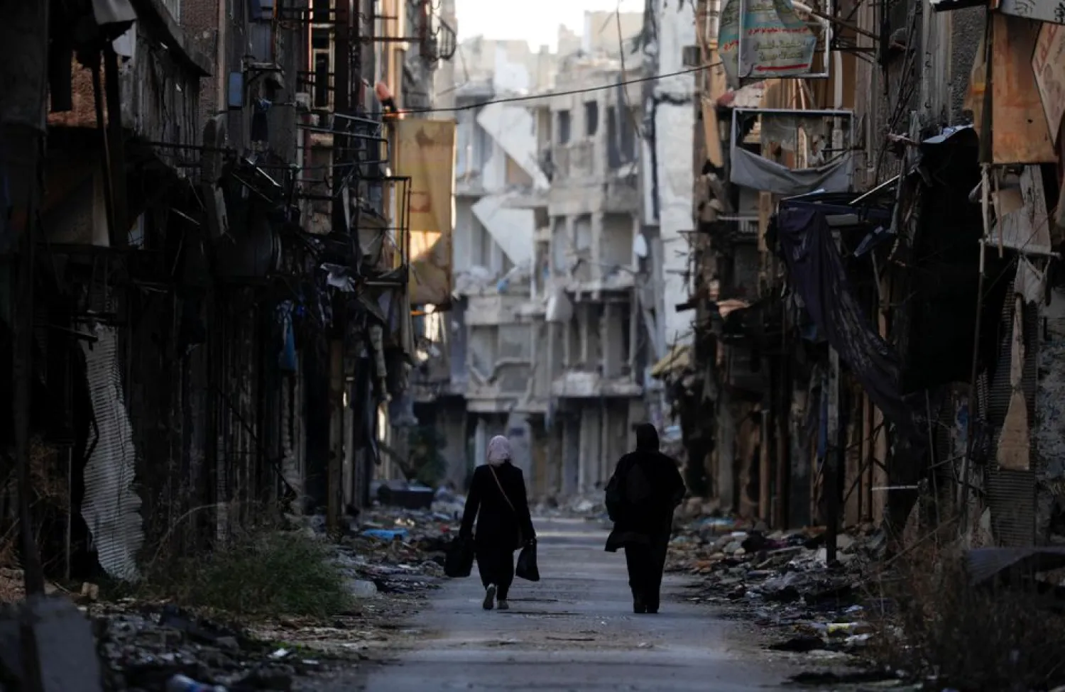 Women walk past damaged buildings at the Yarmouk Palestinian refugee camp on the southern outskirts of Damascus, Syria December 1, 2020. (Reuters)