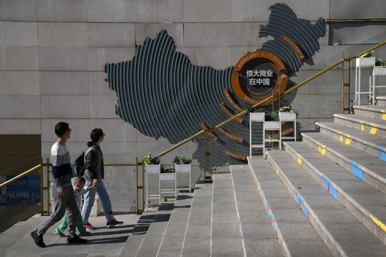 A family walks by a map showing Evergrande development projects in China at an Evergrande city plaza in Beijing, Tuesday, Sept. 21, 2021. (AP Photo/Andy Wong)

