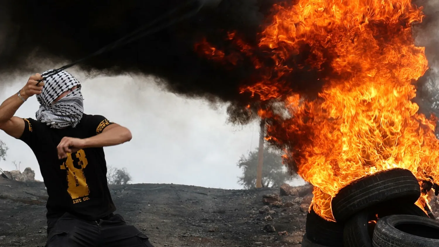 A Palestinian protester hurls rocks from behind burning tires as clashes break out with Israeli troops after a protest against Jewish settlement expansion in the occupied West Bank. (AFP)