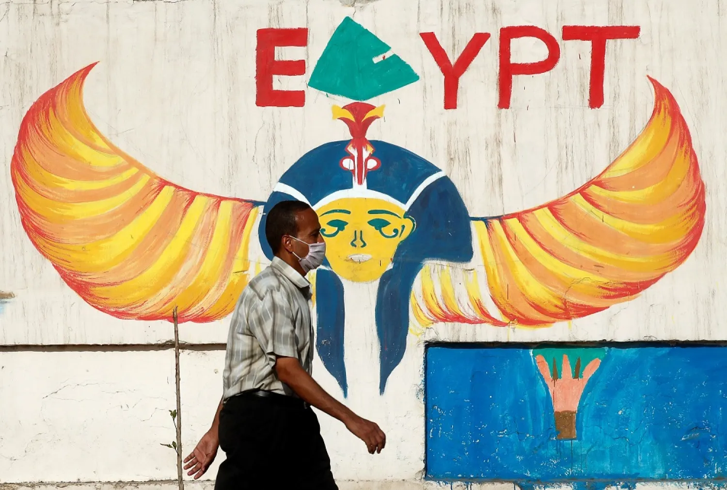 A man wearing a protective face mask walks next to a wall with pharaonic images painted on it, Cairo, June 4, 2020. (Reuters)