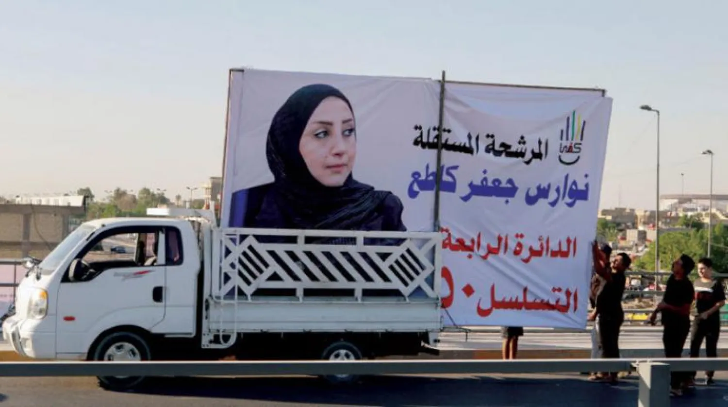 Bağdat’ta bir kadın adayın seçim afişini asmak için çalışan işçiler (Reuters)