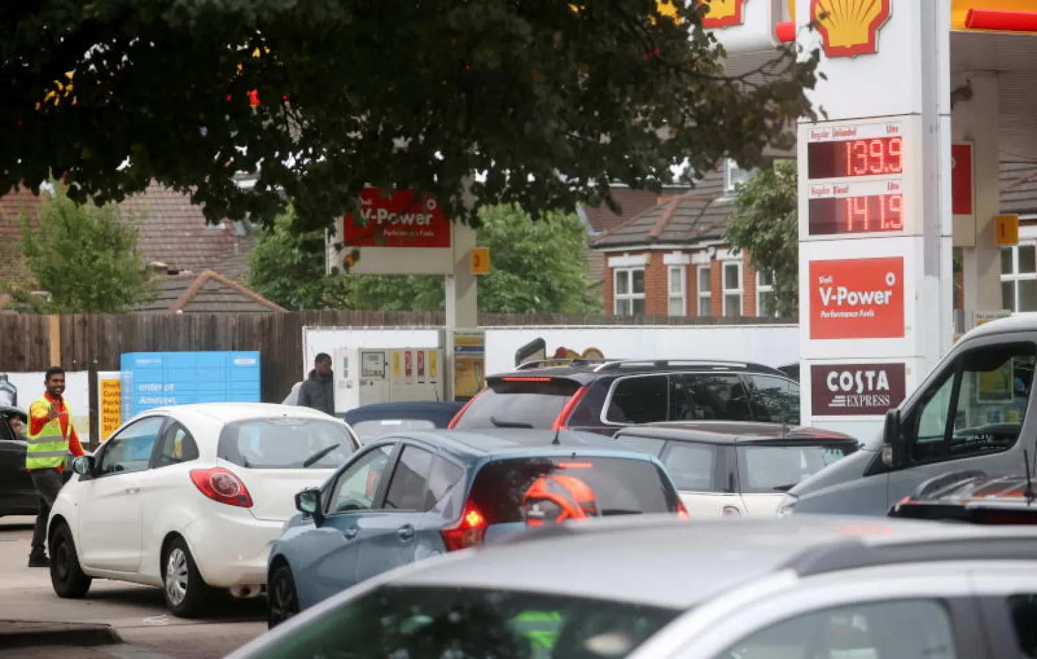 عامل يوجه السيارات أمام محطة وقود في لندن (رويترز)