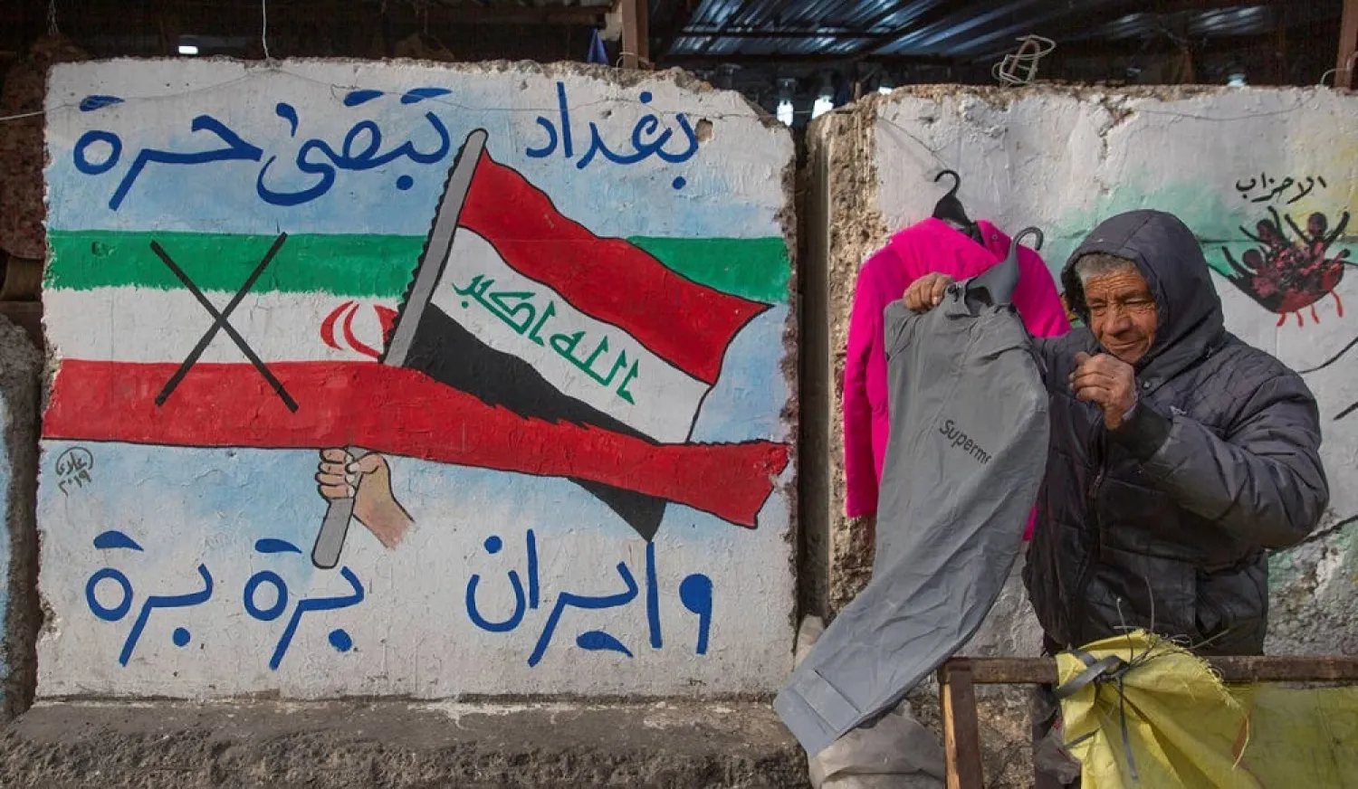 A street vendor displays clothes next to graffiti with Arabic that reads, "Baghdad is free and Iran out," in Tahrir Square, Baghdad, Iraq, January 8, 2020. (AP)