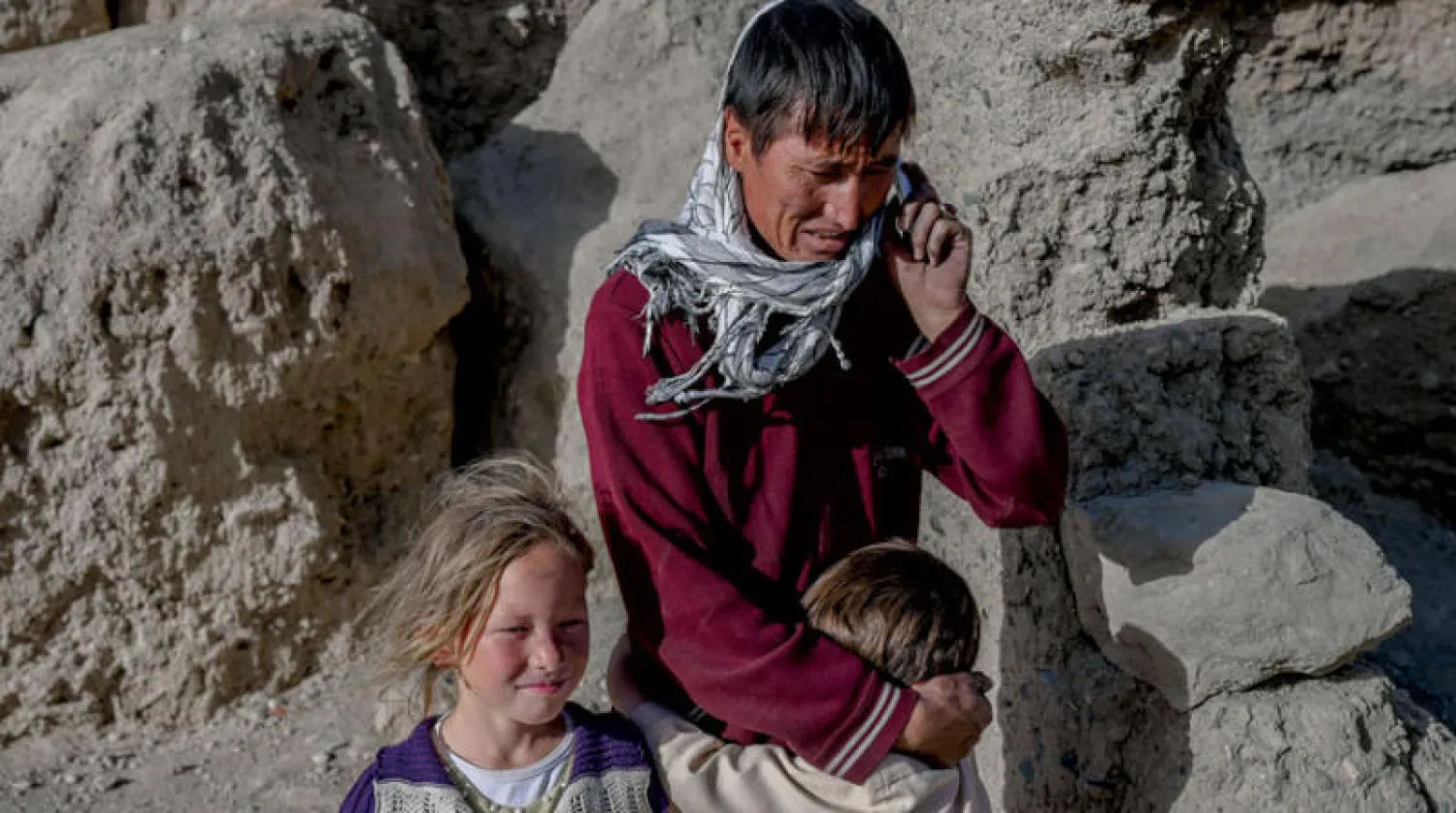 صورة التقطت في 3 أكتوبر 2021 تظهر رجلاً من الهزارة يتحدث على هاتفه الجوال بينما يقف أطفاله بجواره في قريتهم حيث يعيش الناس داخل الكهوف في باميان (أ.ف.ب)