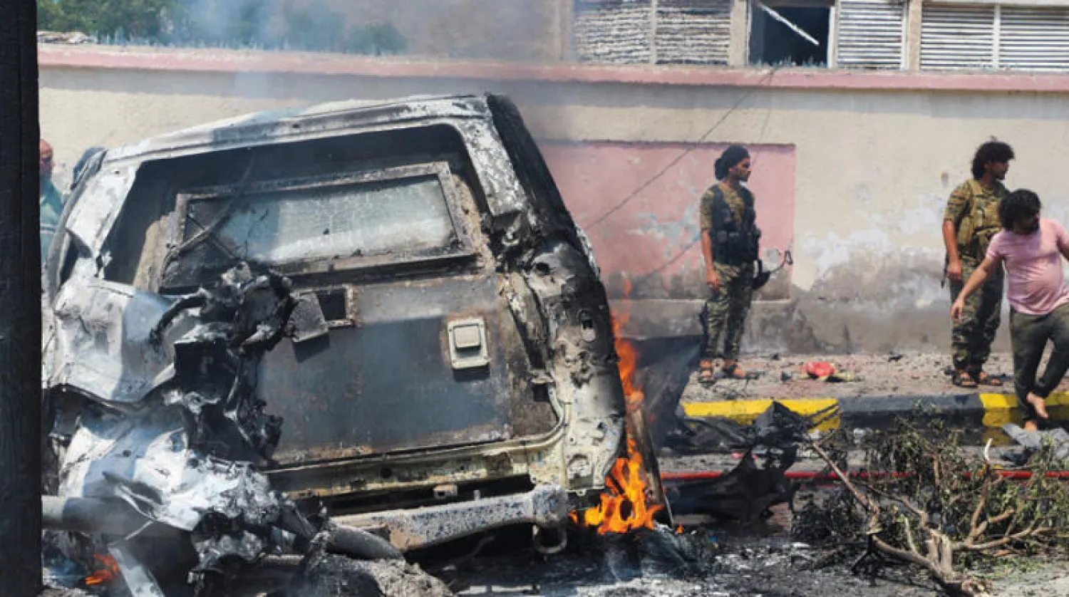 عناصر أمن يعاينون حطام سيارة تحترق كانت ضمن موكب محافظ عدن أحمد لملس أمس (رويترز)