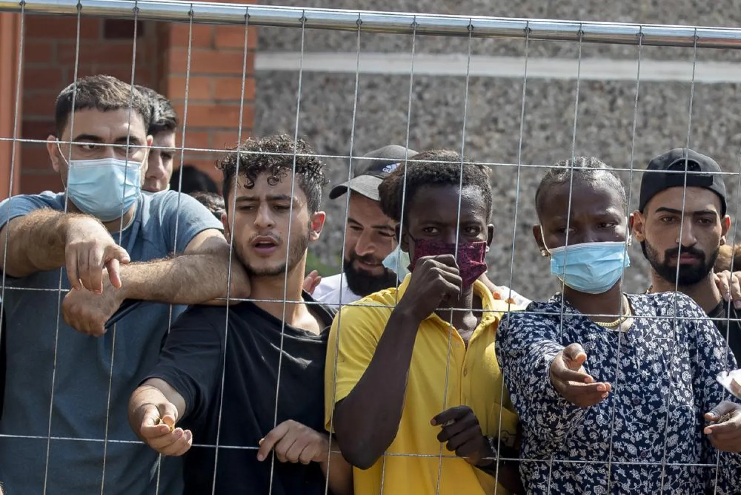 Migrants wait to buy some things standing behind the fence at the refugee camp in the village of Verebiejai, some 145km (99,1 miles) south from Vilnius, Lithuania, Sunday, July 11, 2021.  (AP Photo/Mindaugas Kulbis)
