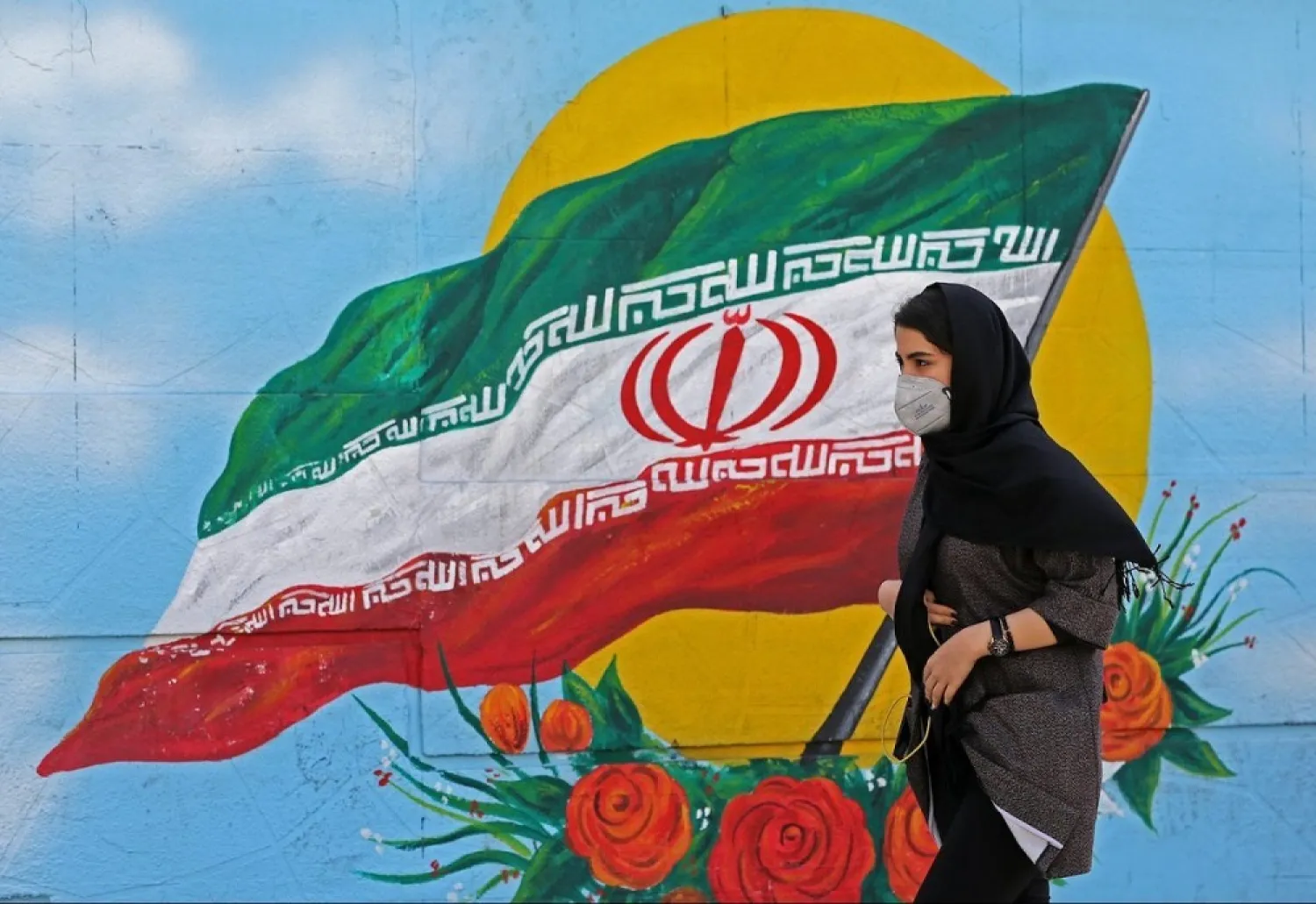 An Iranian woman wearing a mask walks past a mural displaying Iran’s national flag in Tehran, March 4, 2020. (AFP)