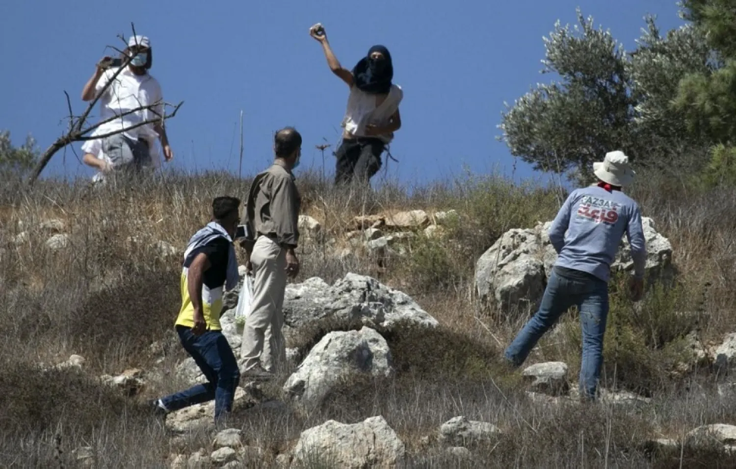 Masked Israeli settlers attack Palestinian olive farmers from the village of Hawara on fields near the settlement of Yitzhar in the Israeli-occupied West Bank, on October 7, 2020. (AFP)
