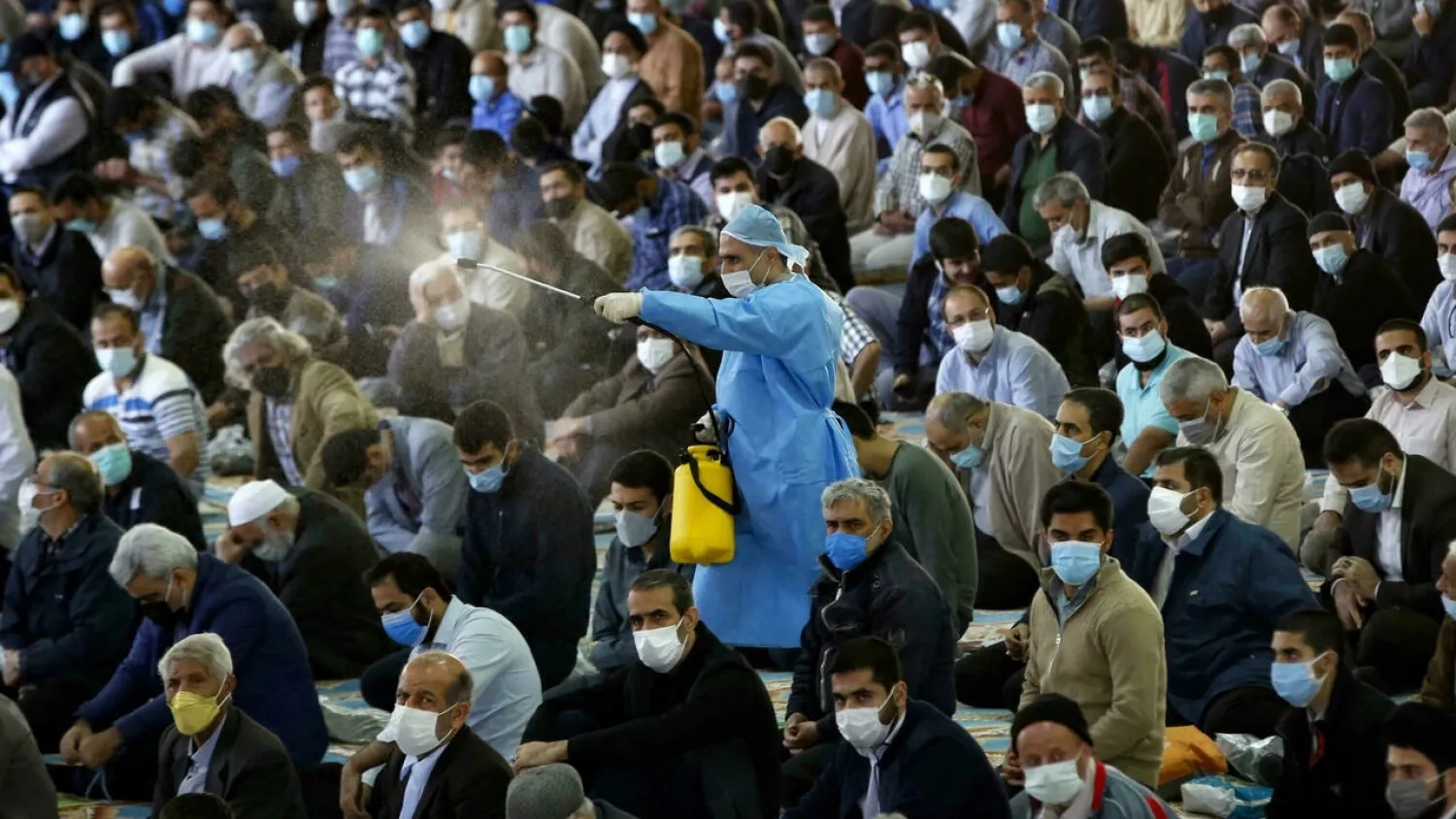 A worker sprays disinfectant as Iranians perform Friday prayers inside a mosque in Tehran for the first time in 20 months. (AFP)