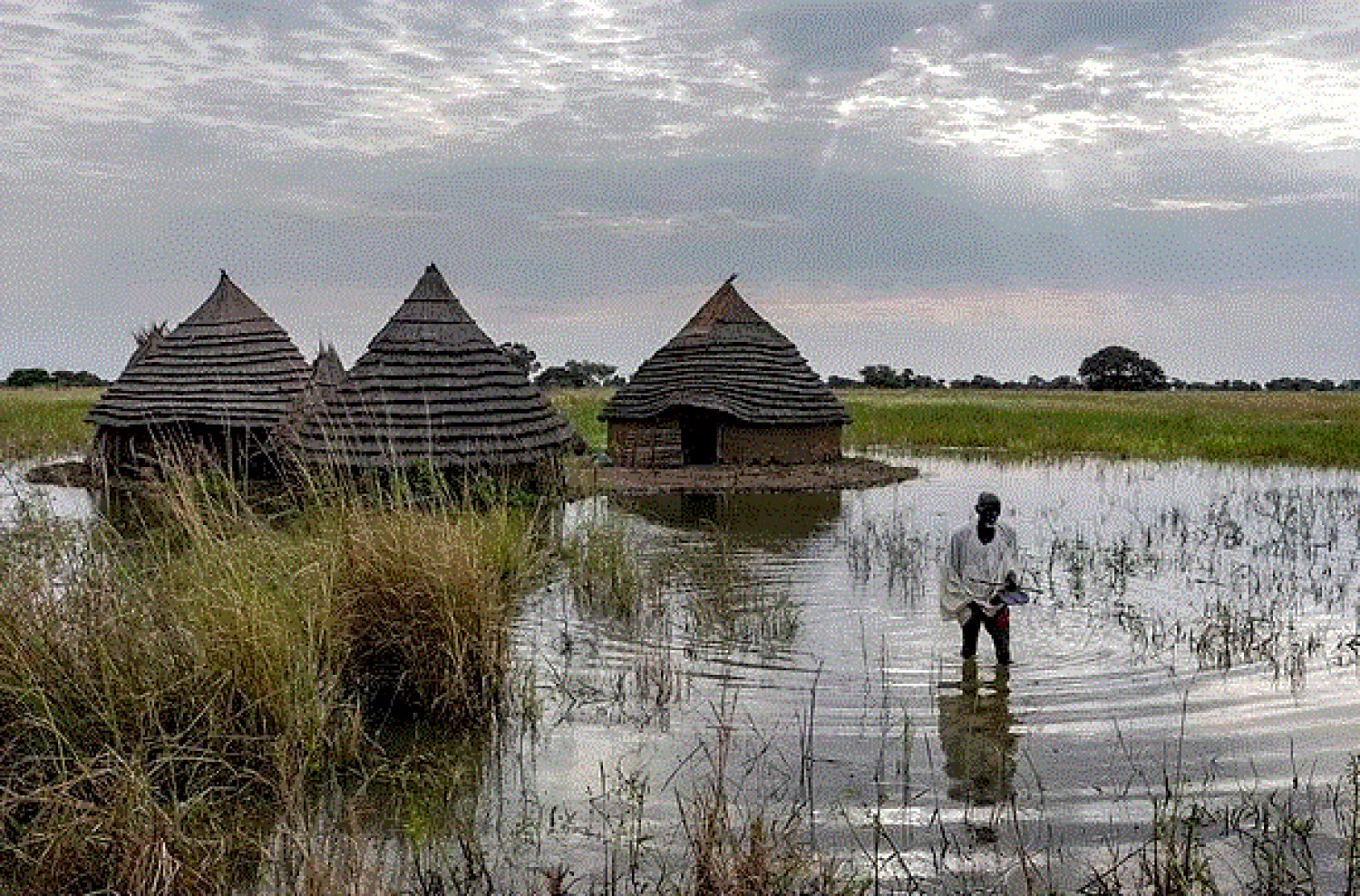 Yel Aguer Deng, who does not know his age, walks through water from his compound to the Wanyhok-Akon road, near Malualkon in Northern Bahr el Ghazal State, South Sudan, Wednesday, Oct. 20, 2021. (AP Photo/Adrienne Surprenant)

