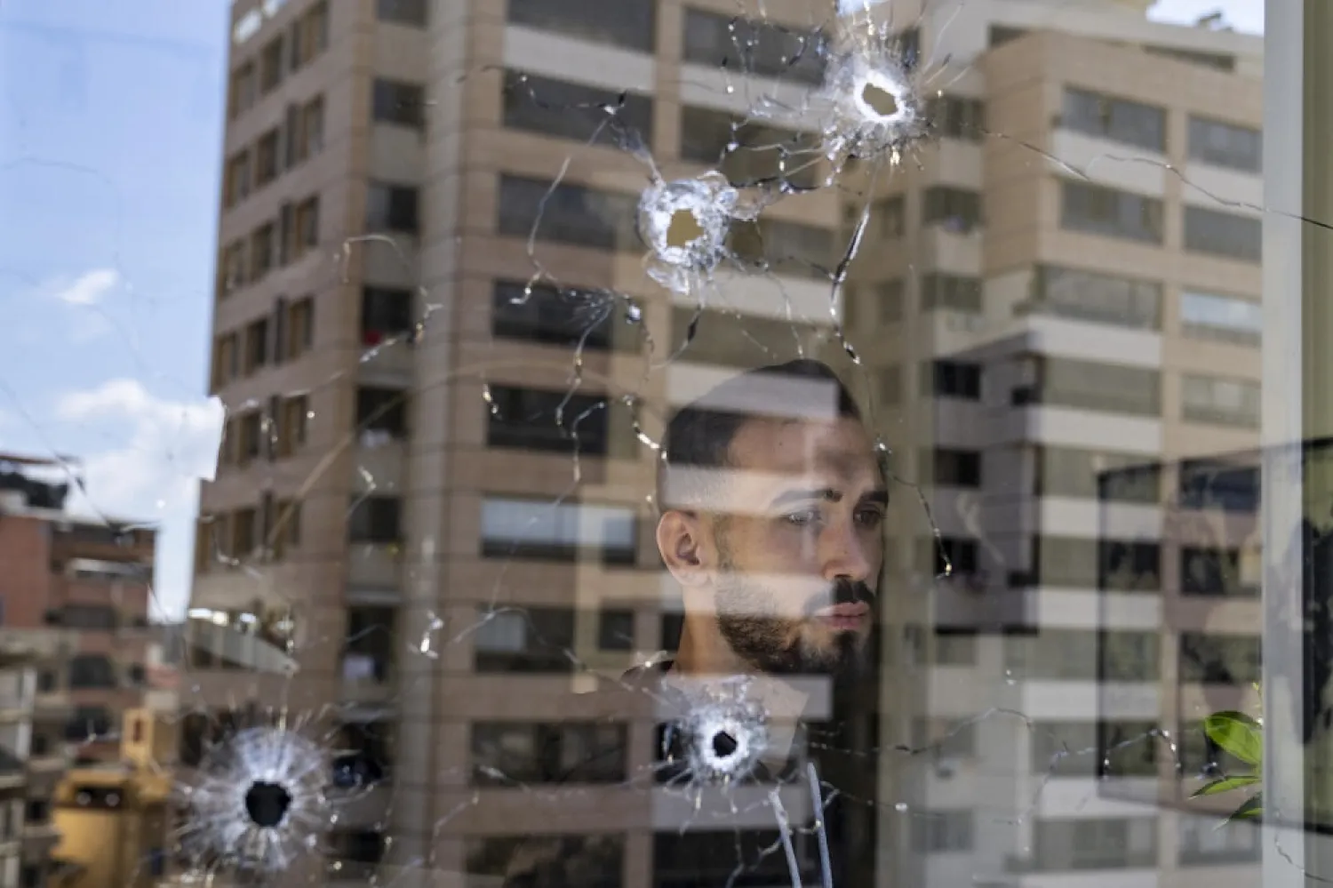 An employee looks through an office window riddled with bullet holes after the deadly clashes that erupted in Tayyouneh, Beirut, Lebanon, Tuesday, Oct. 19, 2021. (AP)