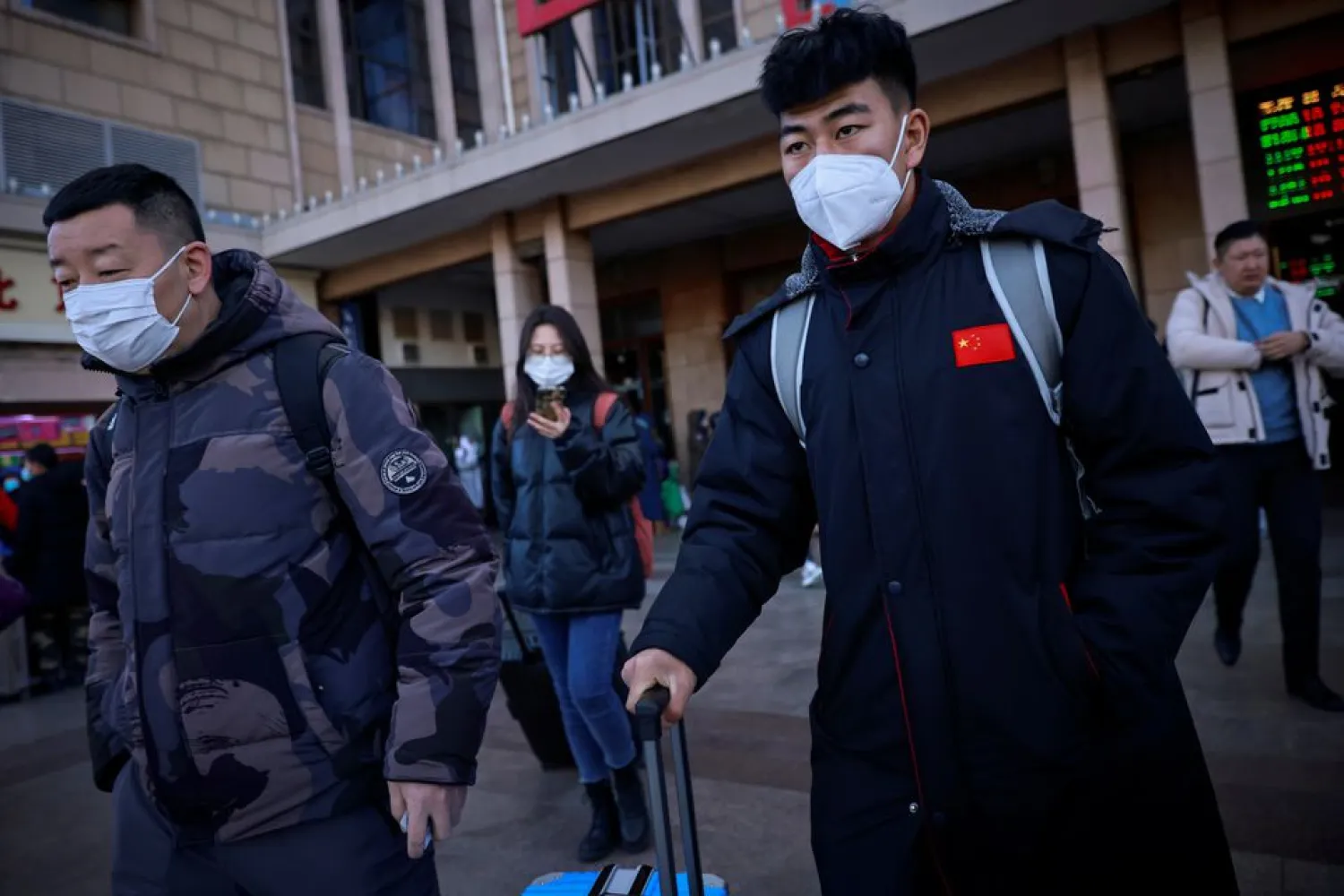Travelers wearing face masks push suitcases outside Beijing Railway Station following an outbreak of the coronavirus disease (COVID-19) in Beijing, China, December 29, 2020. REUTERS/Thomas Peter