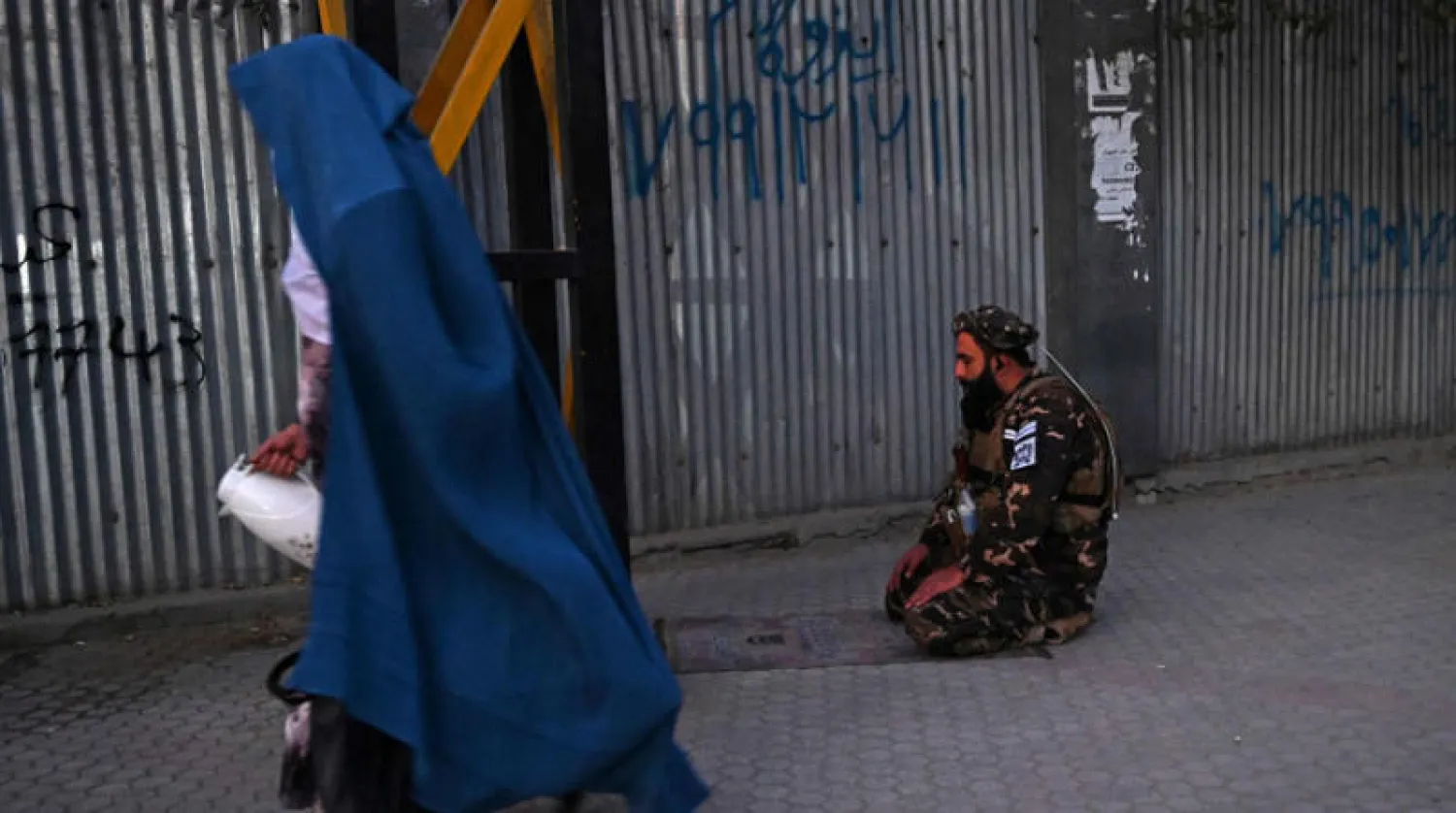 امرأة أفغانية تمر بجانب عنصر من «طالبان» يؤدي الصلاة في شارع قرب مستشفى عسكري تعرض لاعتداء إرهابي في كابل أمس (أ.ف.ب)