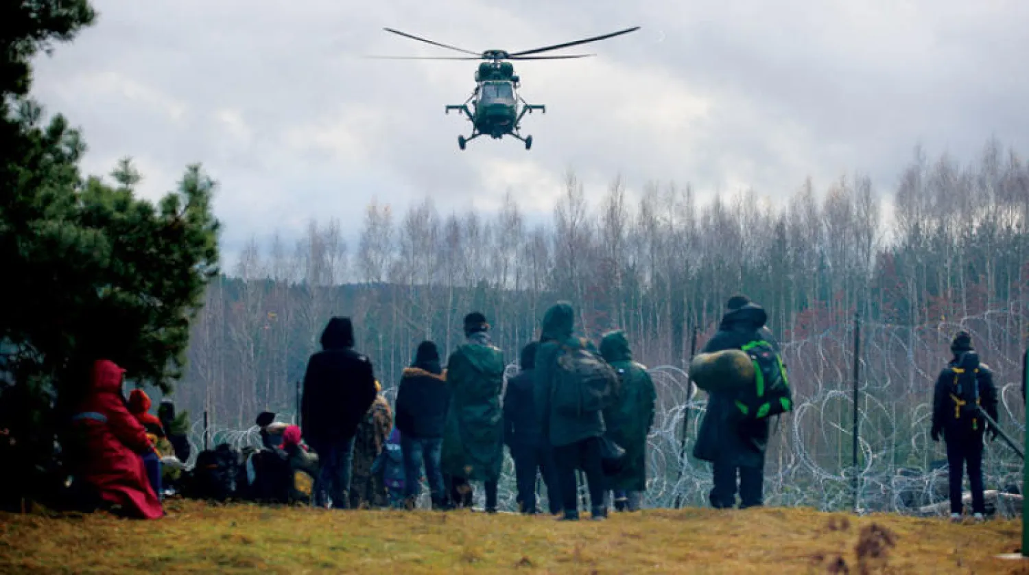 مهاجرون يتجمعون قرب سياج من أسلاك شائكة بمنطقة غرودنو في بيلاروسيا محاولين العبور إلى بولندا أمس (رويترز)