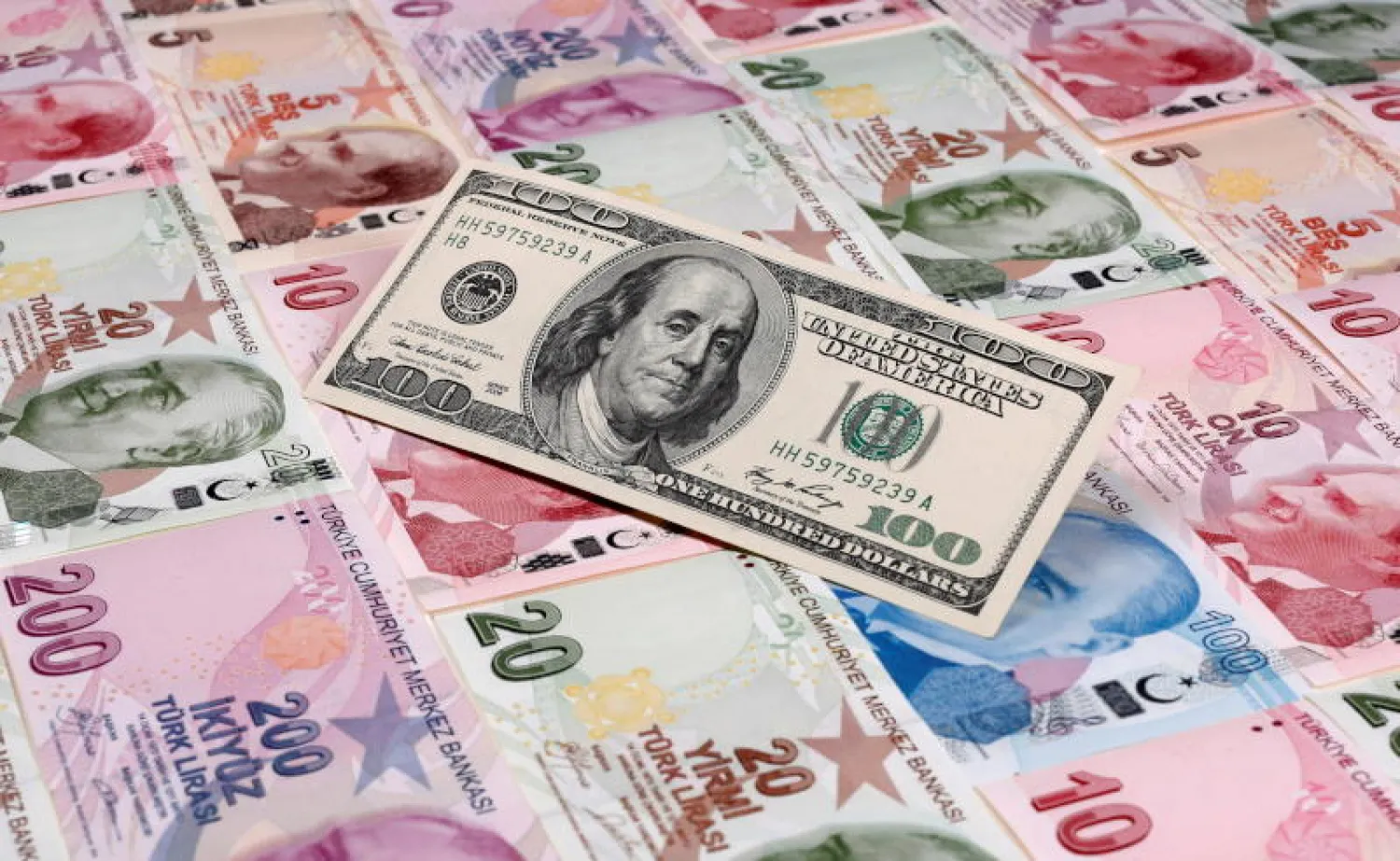 عملة ورقية من فئة 100 دولار أميركي تظهر فوق أوراق من الليرة التركية (رويترز)