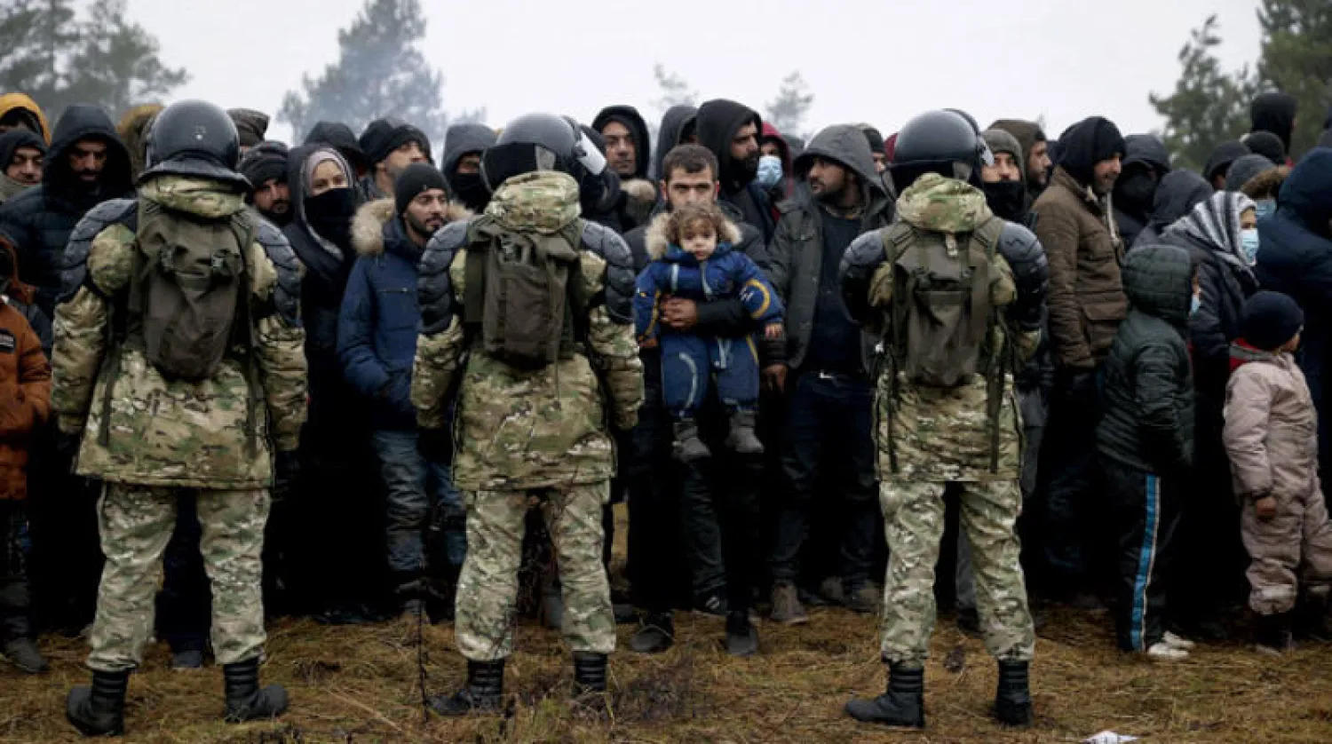 جنود يقفون أمام مهاجرين في مخيم على حدود بيلاروسيا وبولندا أمس (أ.ف.ب)