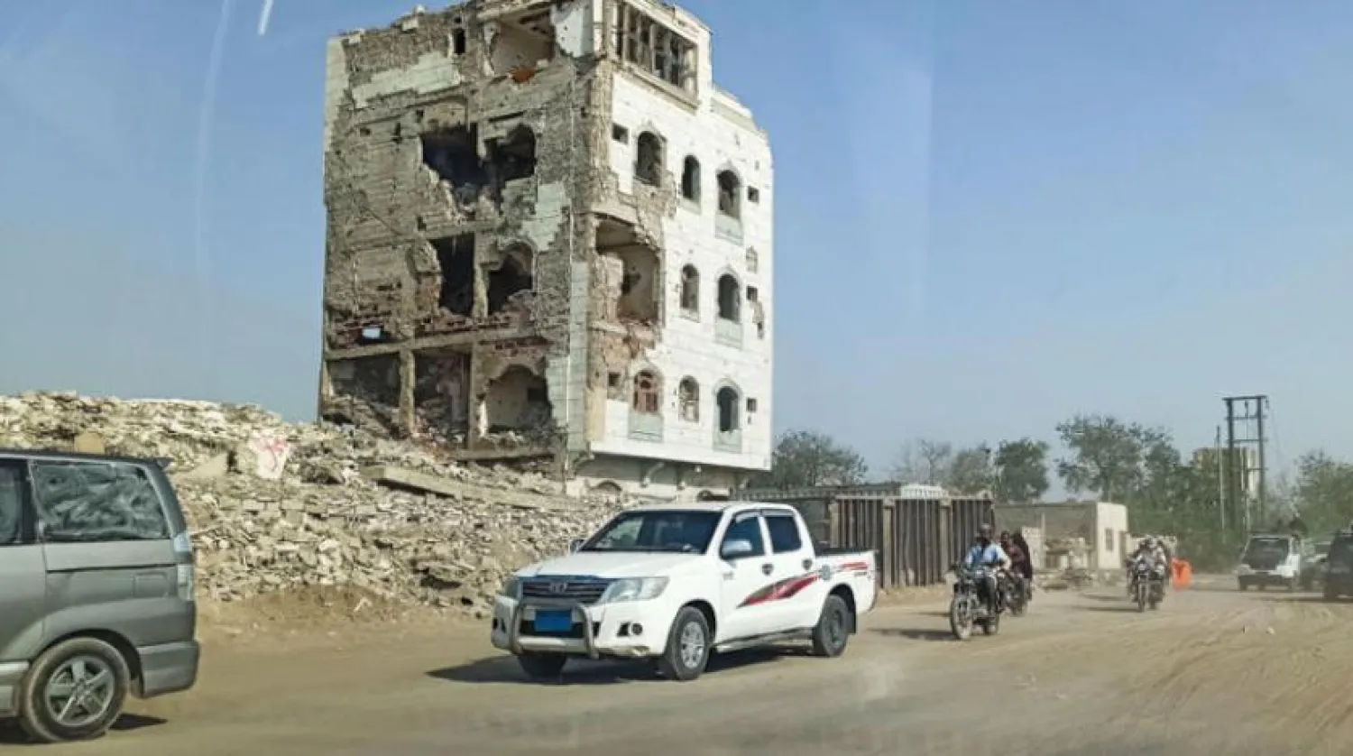 Hudeyde kentindeki savaşın ardından yıkılan bir binanın önünden arabalar ve motosikletler geçiyor (Reuters)
