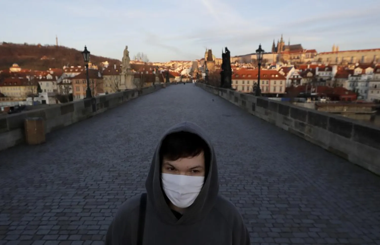 FILE - In this March 16, 2020 file photo a young man wearing a face mask walks across an empty Charles Bridge in Prague, Czech Republic.  (AP Photo/Petr David Josek, File)
