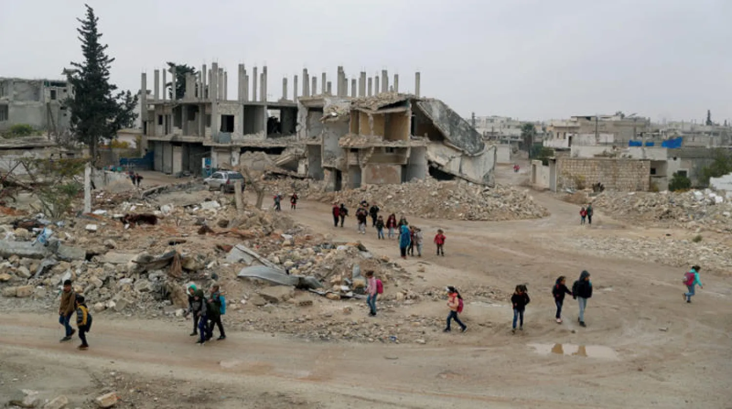 تلاميذ سوريون يمرون بجوار أبنية هدمتها غارات جوية في طريقهم إلى مدرستهم ببلدة النيرب بريف حلب يوم الأحد (د.ب.أ)