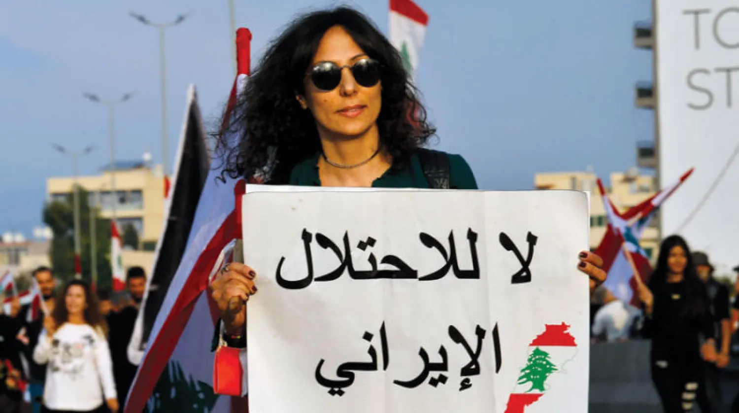 محتجة ترفع لافتة ضد النفوذ الإيراني خلال عرض بمناسبة ذكرى استقلال لبنان في بيروت أمس (أ.ب)
