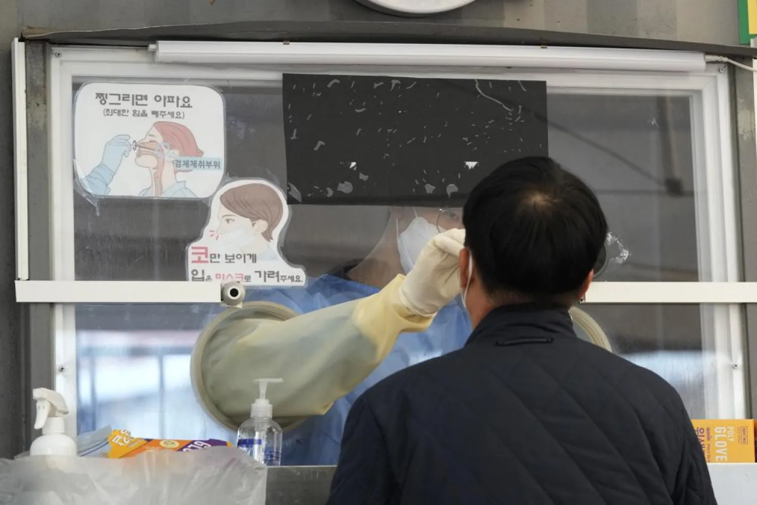 A medical worker in a booth takes a nasal sample from a man at a makeshift testing site in Seoul, South Korea, Wednesday, Nov. 24, 2021. (AP Photo/Ahn Young-joon).
