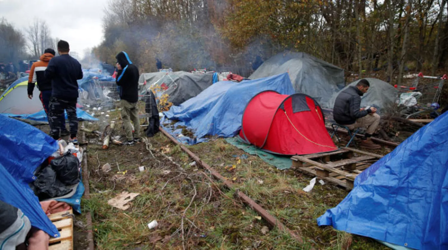 مهاجرون أمام خيام في منطقة لون بيتش قرب كاليه بفرنسا أمس (رويترز)