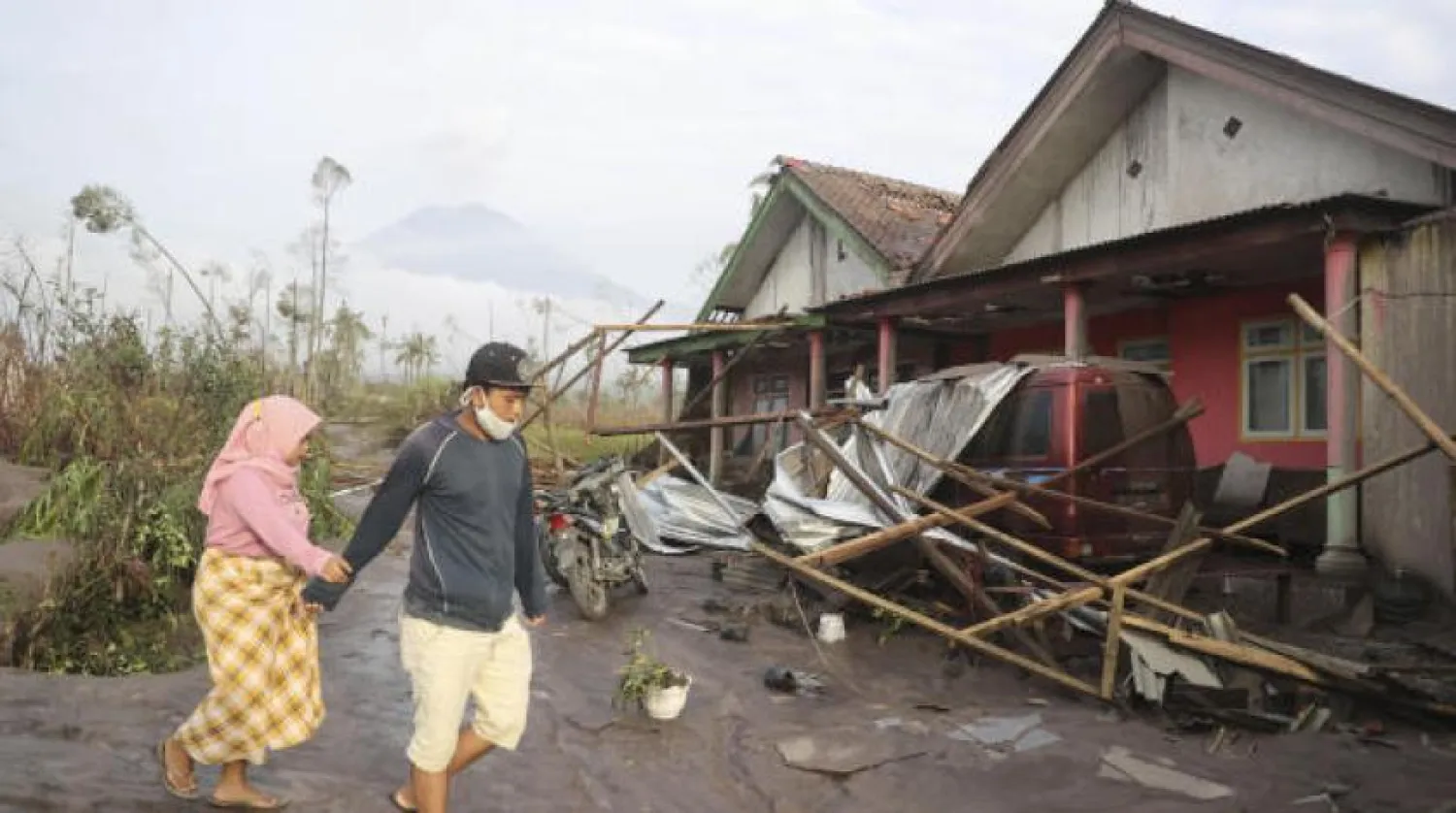 Köylüler, Semeru yanardağının patlamasından etkilenen bir bölgede yıkılan evlerinin yakınında yürüyorlar. (AP) 
