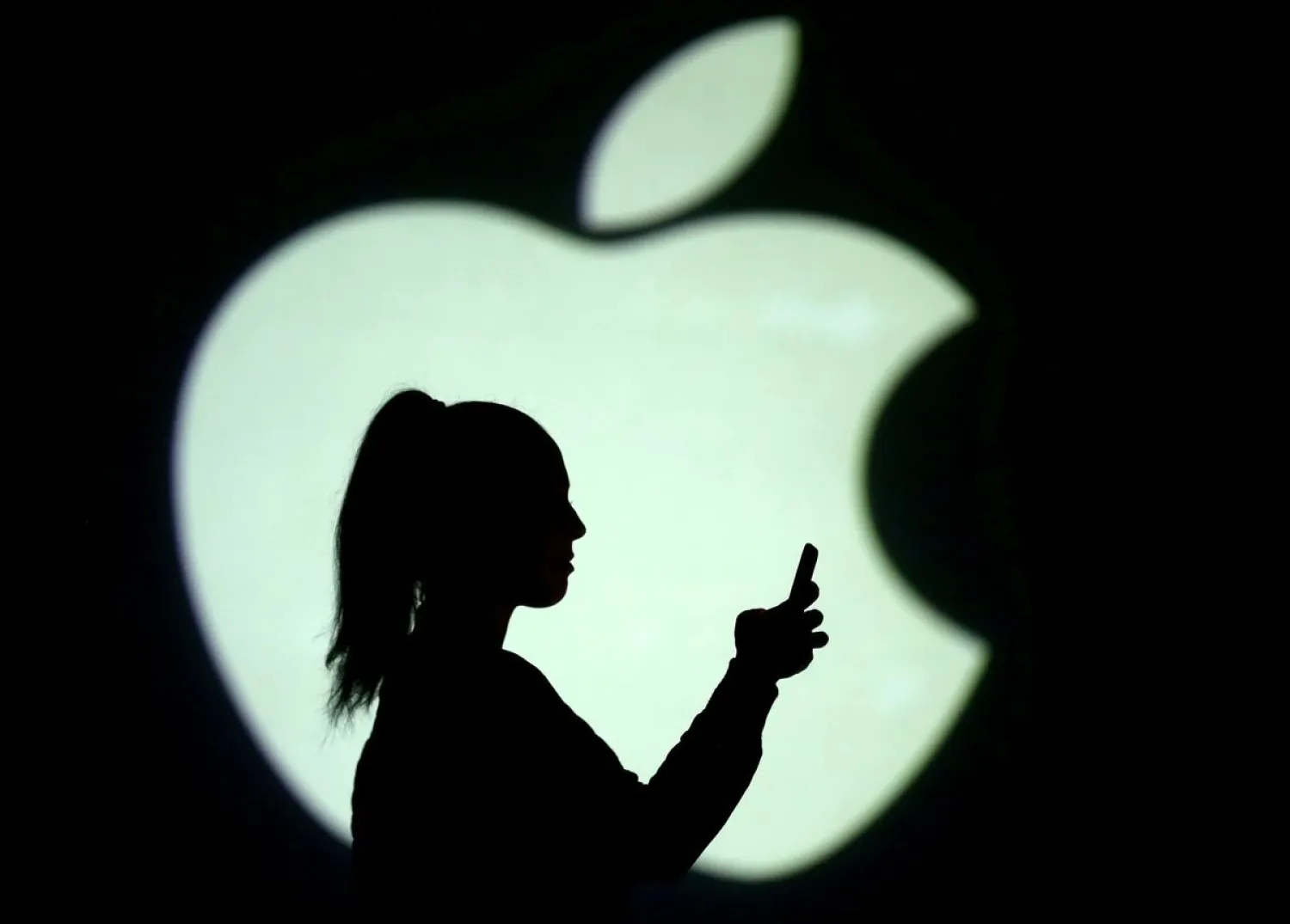 Silhouette of a mobile user seen next to a screen projection of the Apple logo in this picture illustration taken March 28, 2018. (Reuters)
