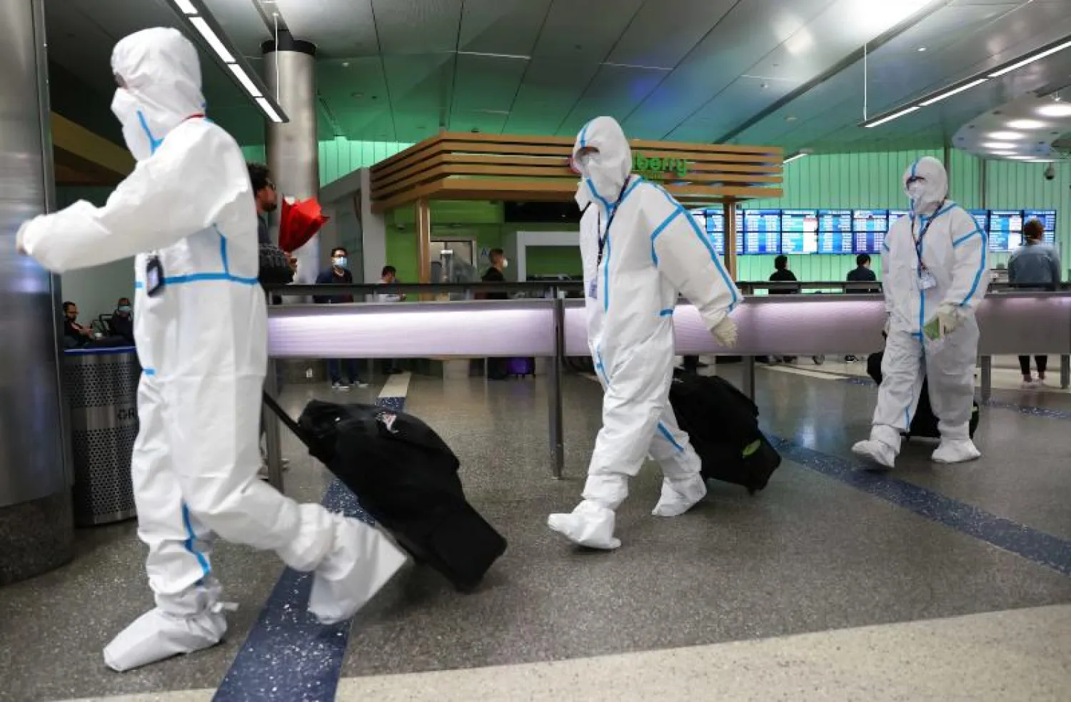 مسافرون يرتدون البدلات الواقية للحماية من فيروس كورونا في مطار لوس أنجليس الدولي (أ.ف.ب)