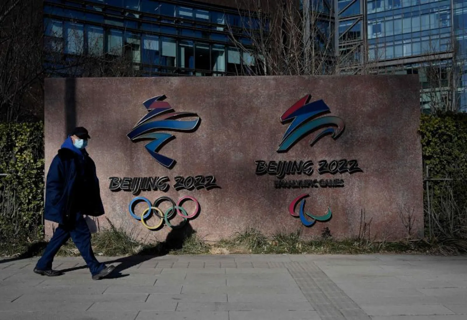رجل يسير الى جانب شعار الألعاب الأولمبية الشتوية في بكين (أ.ف.ب)